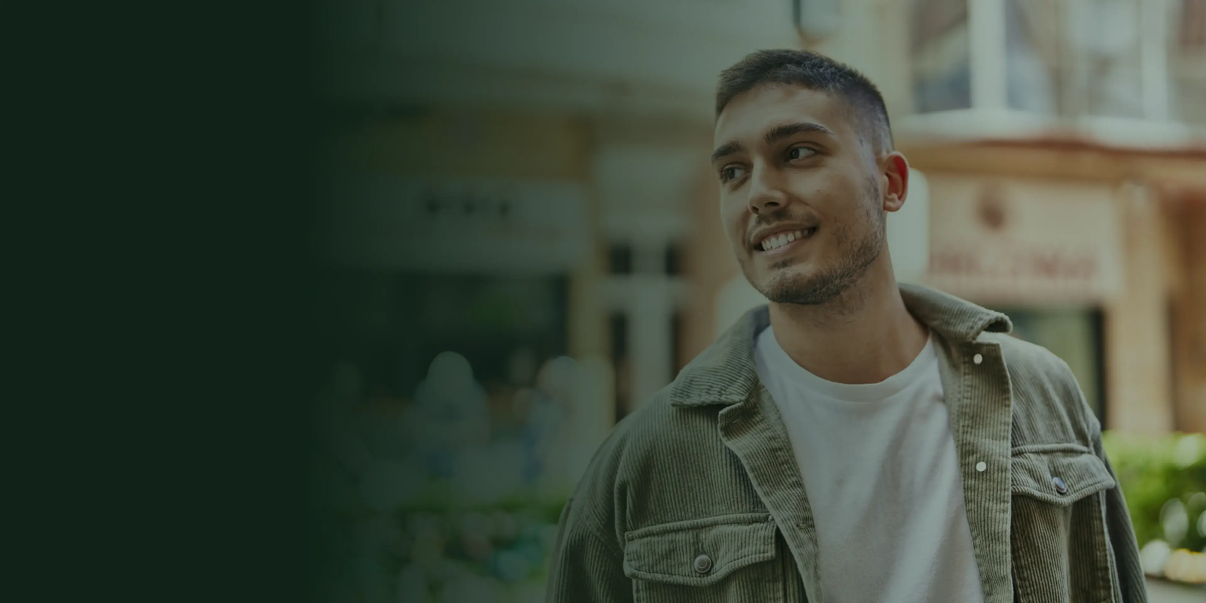 A man in a jacket smiles while looking to the side, standing outdoors.
