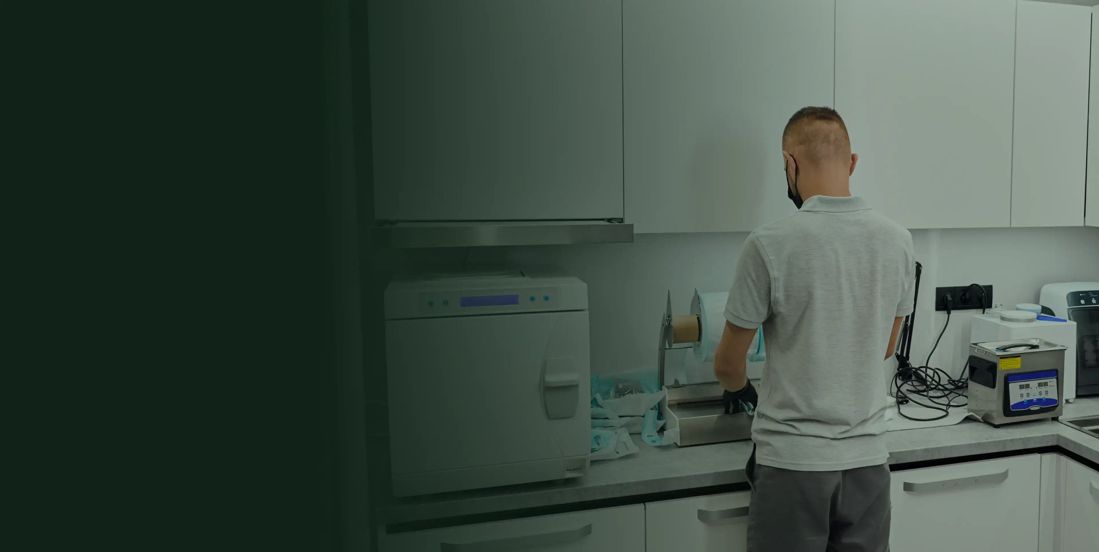 Man wearing a gray shirt working in a kitchen area with white cabinets and tech equipment.