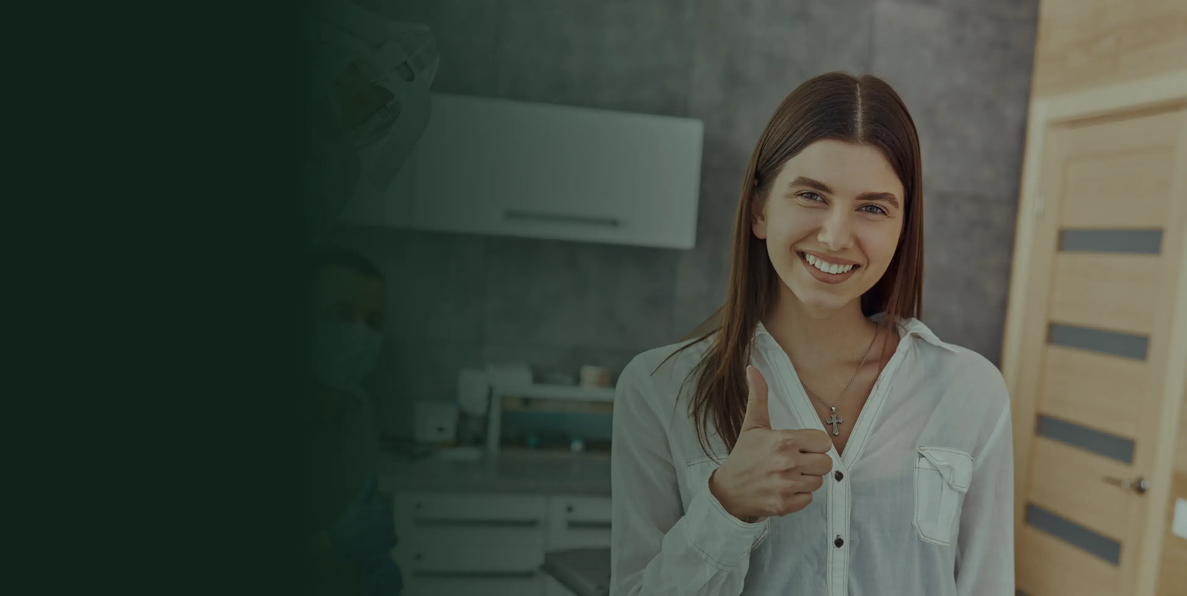 A woman in a white shirt smiling and giving a thumbs-up in a kitchen setting.