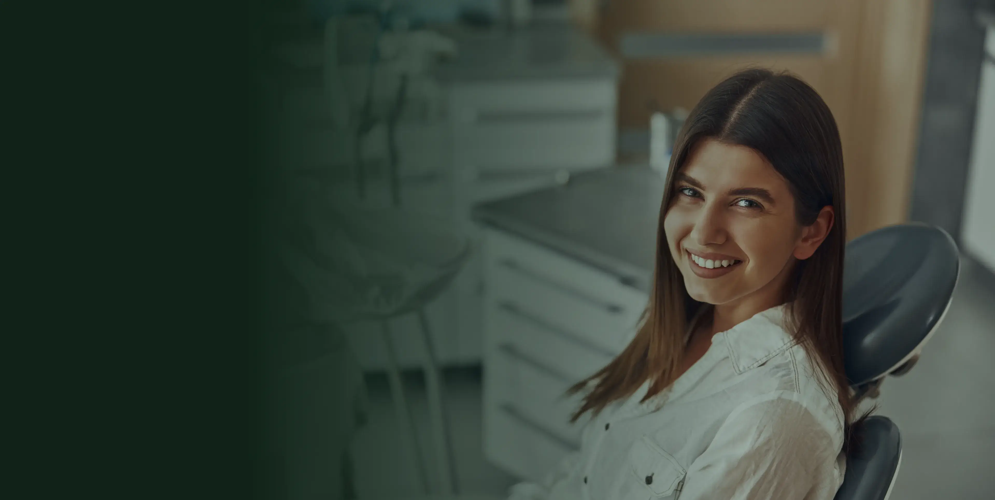 A woman sitting in a dental chair, smiling at the camera.