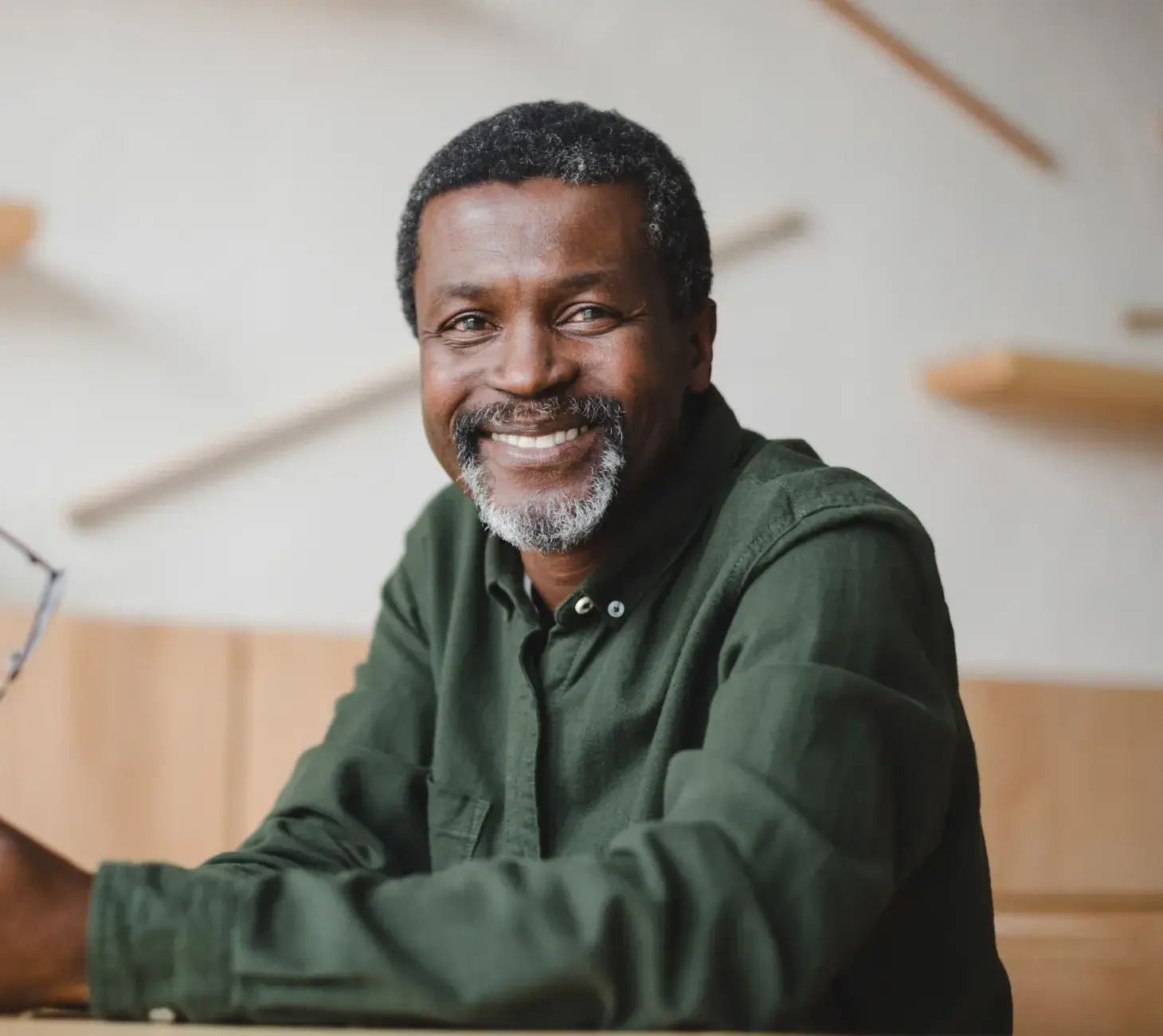 A man in a green shirt smiles while sitting indoors.