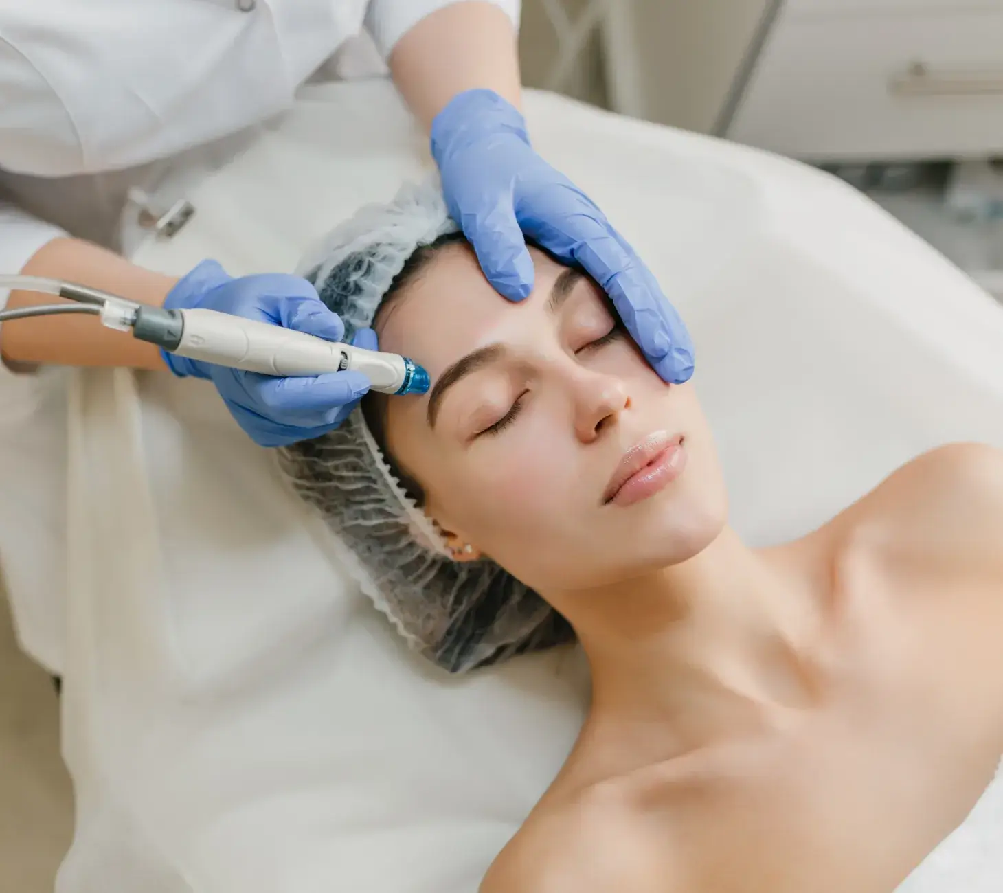 A woman receives a facial treatment with a machine, guided by a professional wearing blue gloves.