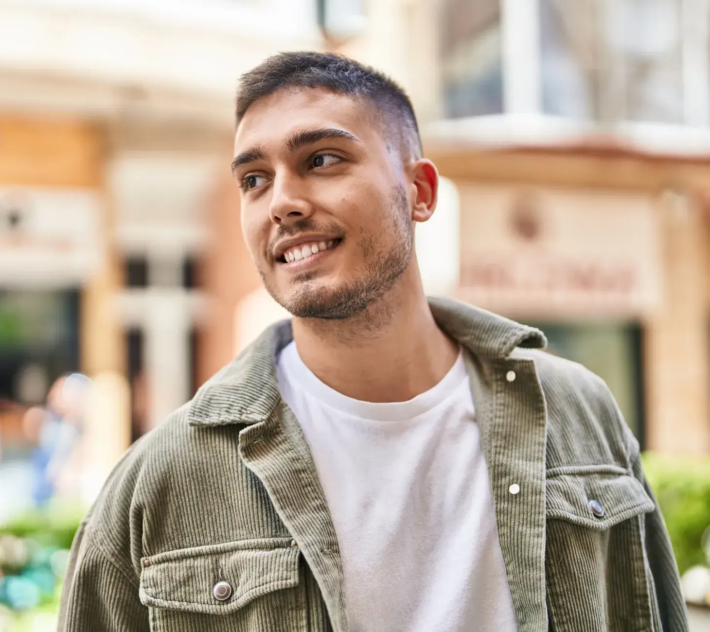 A person smiling while standing outdoors, wearing a green jacket and white shirt.