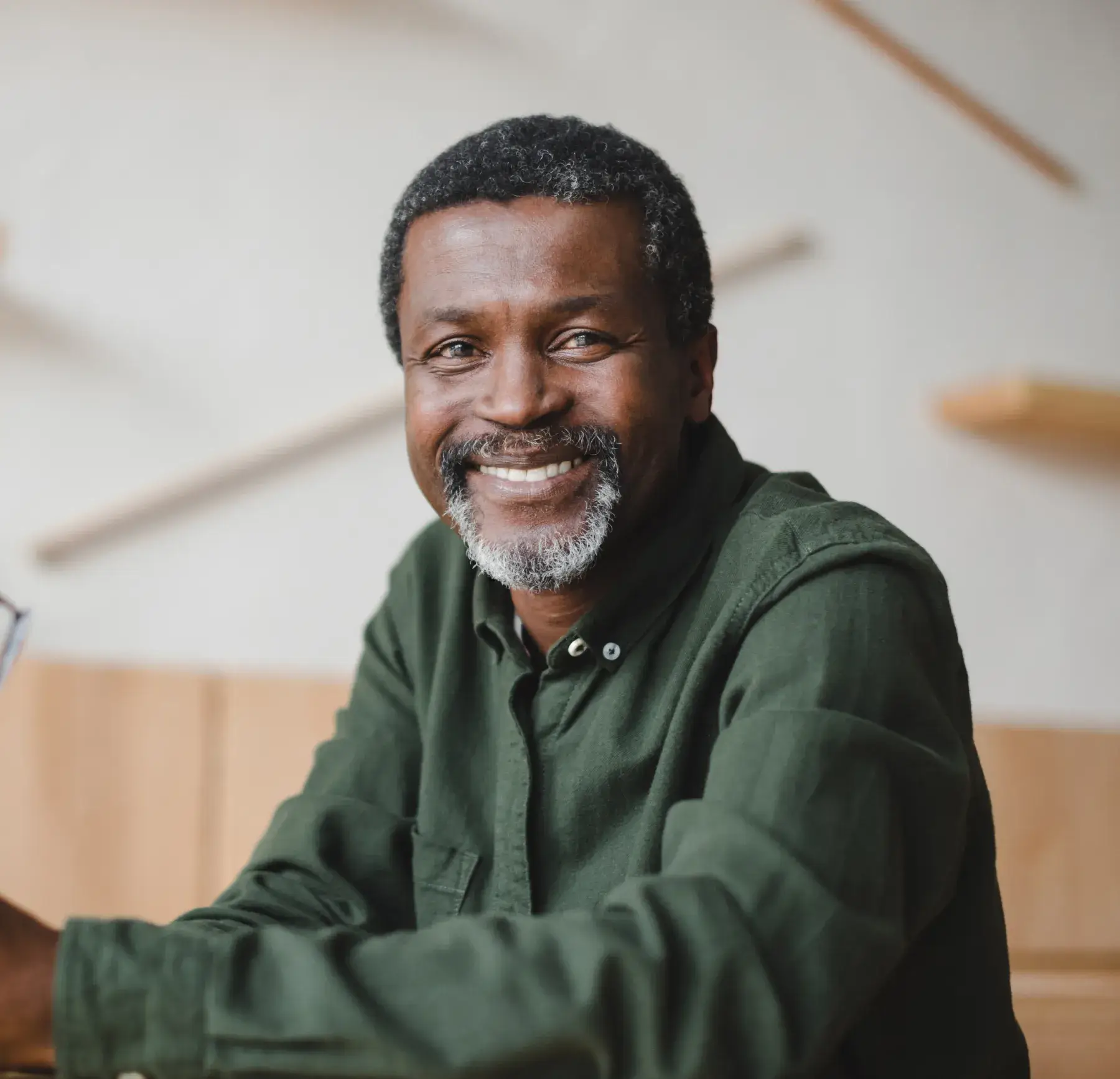 Man in a green shirt smiling while sitting at a table indoors.
