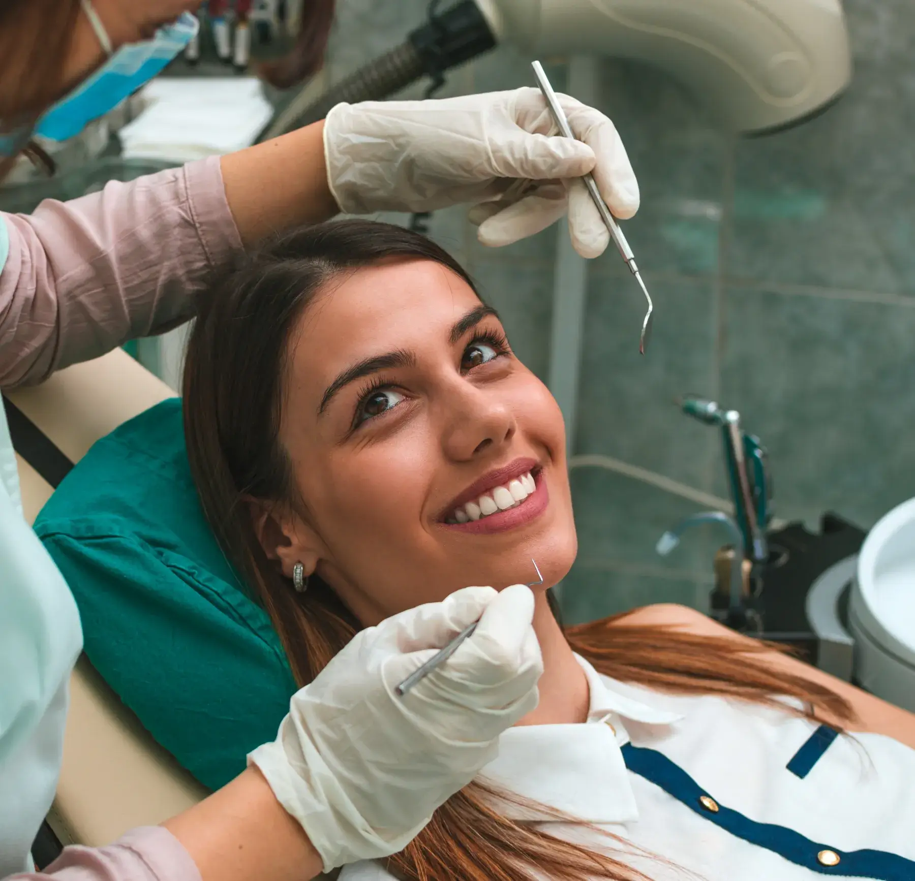 Dentist examines smiling woman's teeth with dental tools in an office.