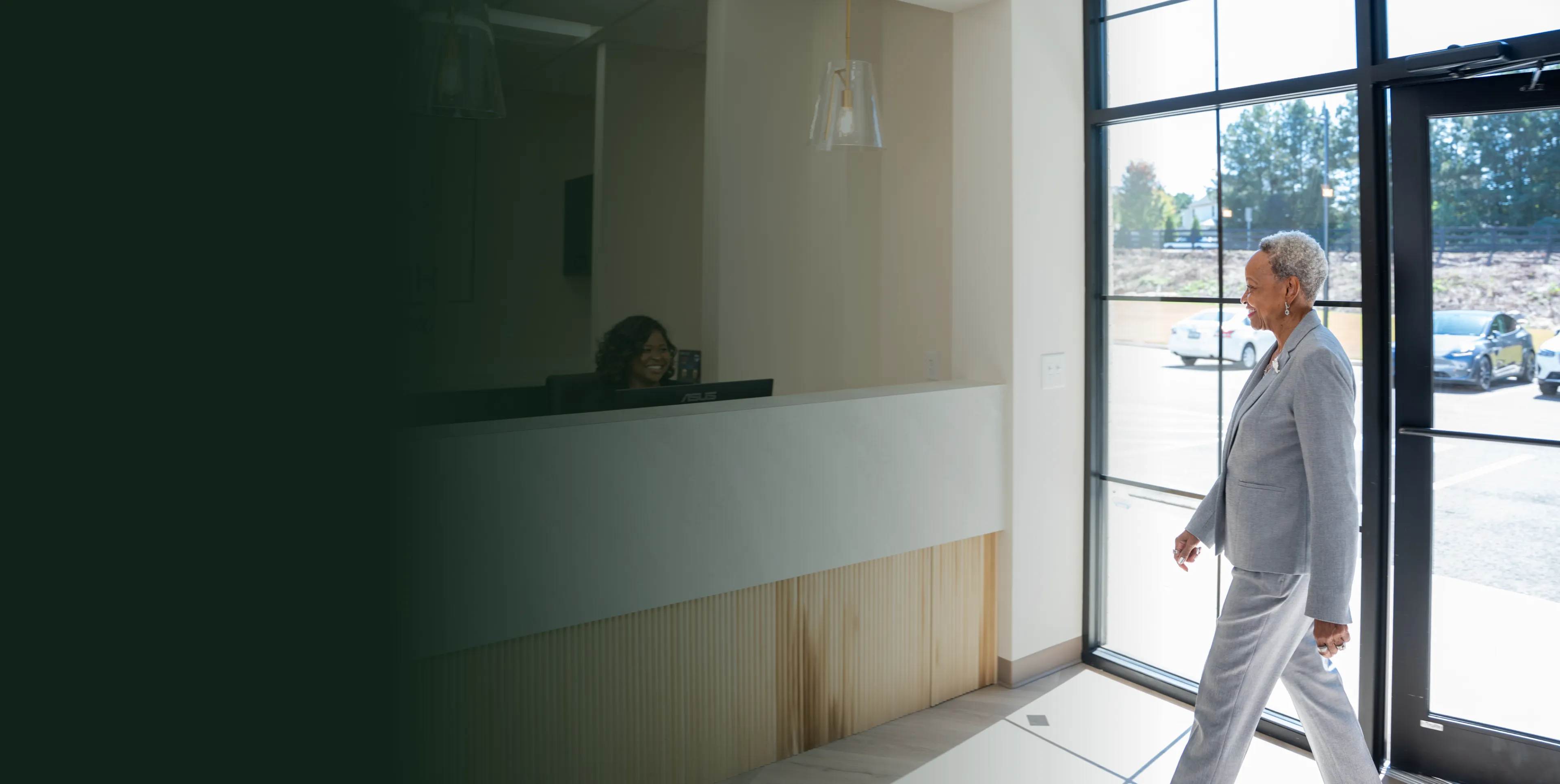 An older adult walks through a glass door into a bright room with a reception desk.