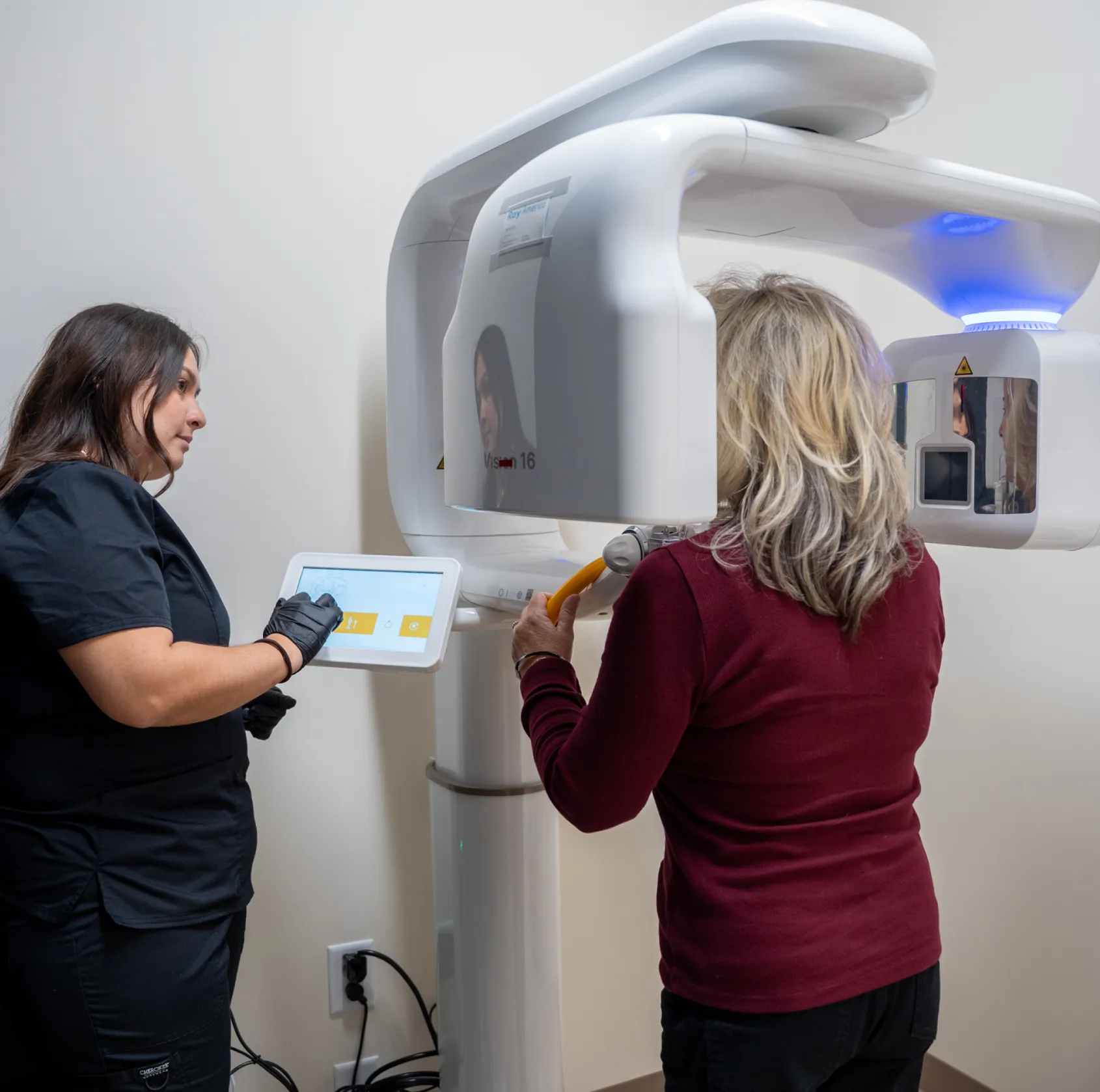A dental technician assists a patient using a 3D imaging machine for a dental scan.
