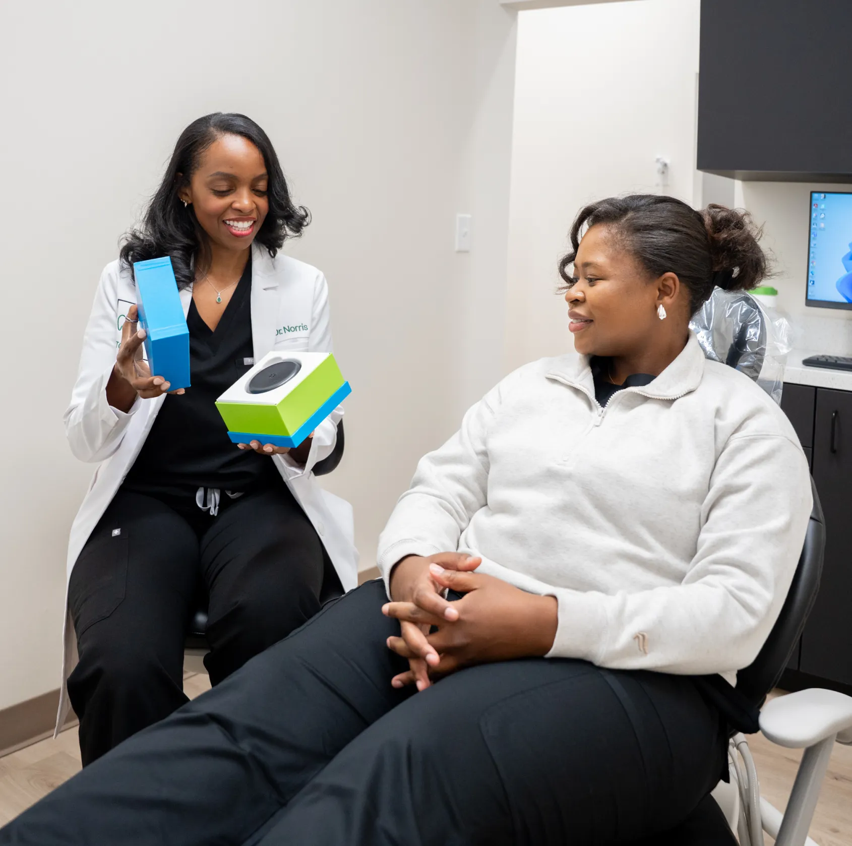A dentist shows a patient how to use a dental care product during an appointment.