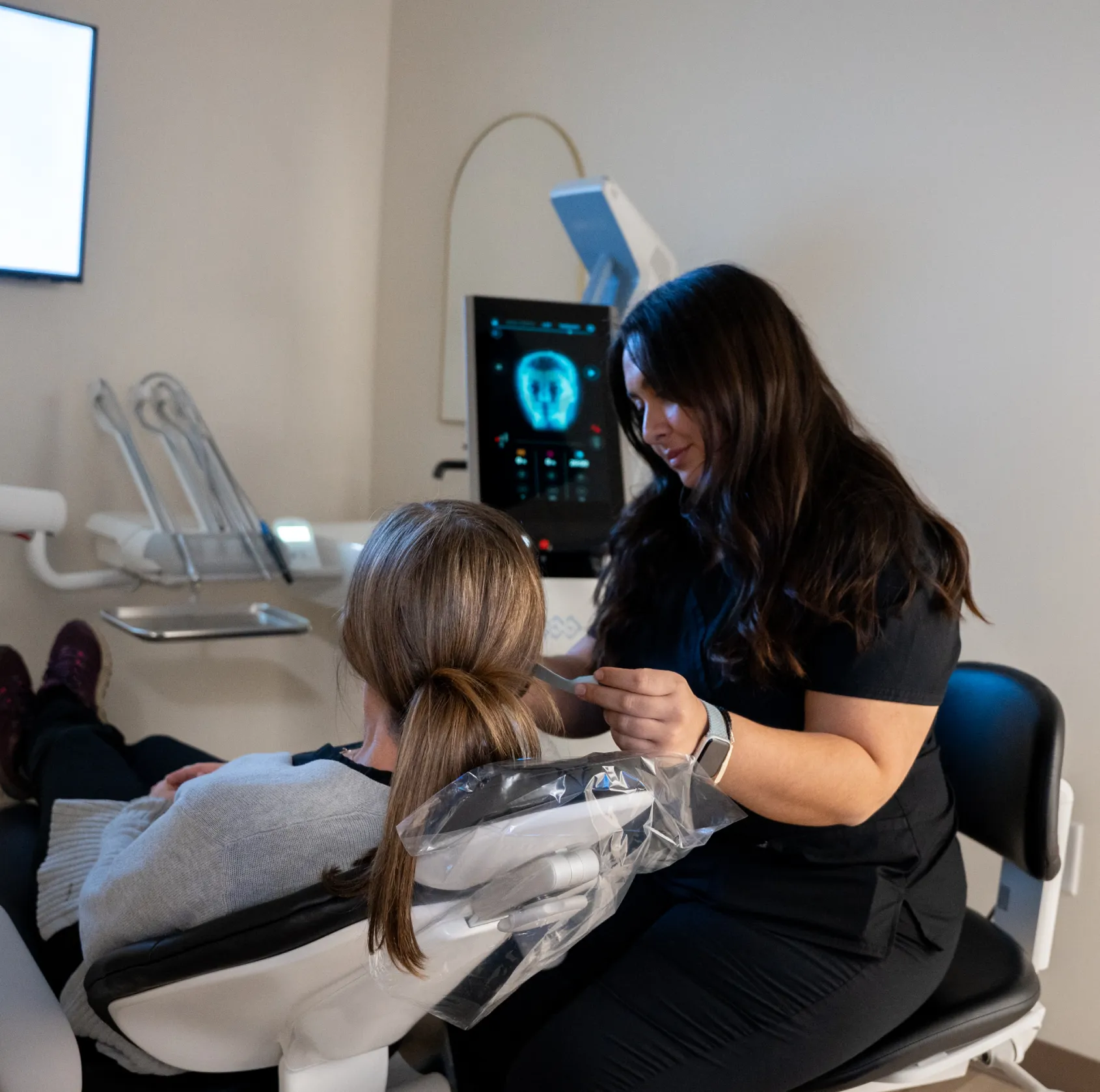 A dental professional examines a patient seated in a dentist's chair.