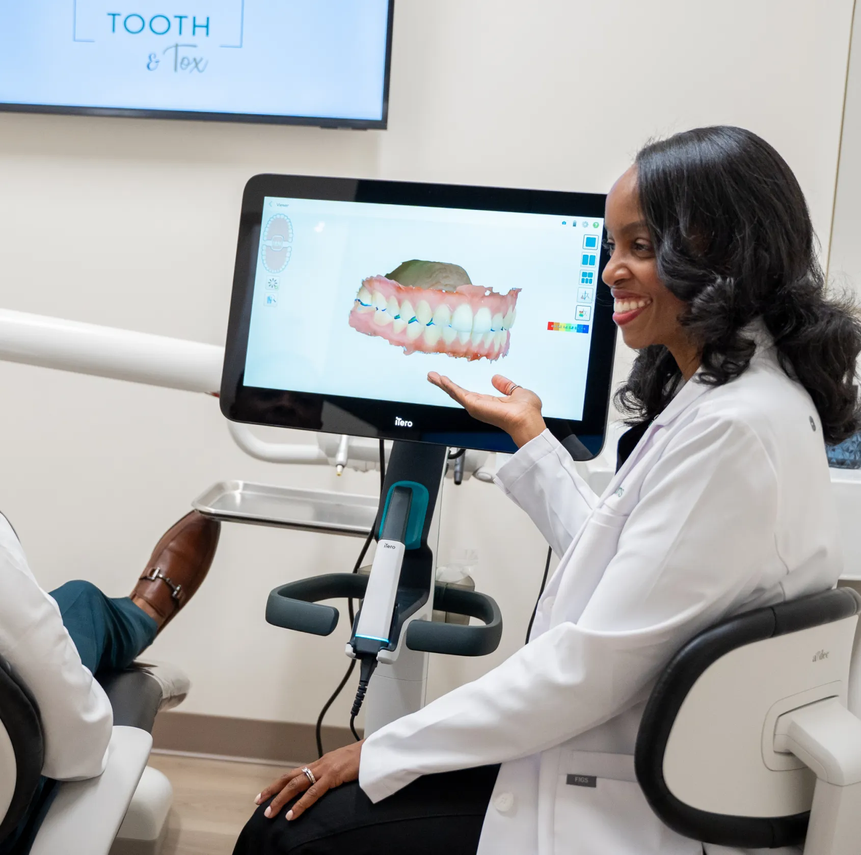 A dentist explains a digital 3D scan of teeth displayed on a computer screen to a patient.
