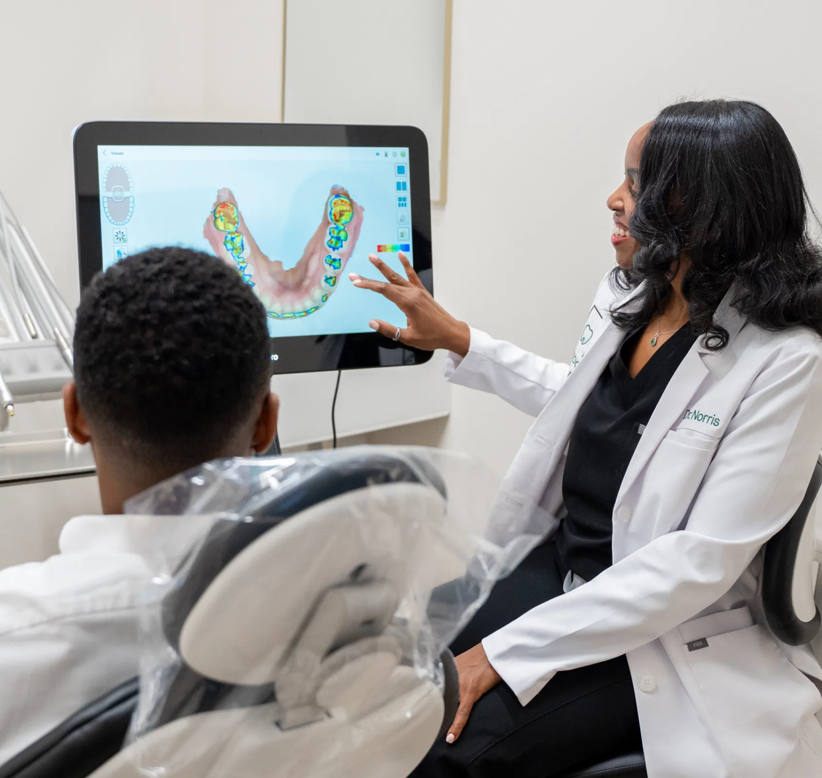 A dentist shows a patient a digital image of teeth on a screen in a dental office.