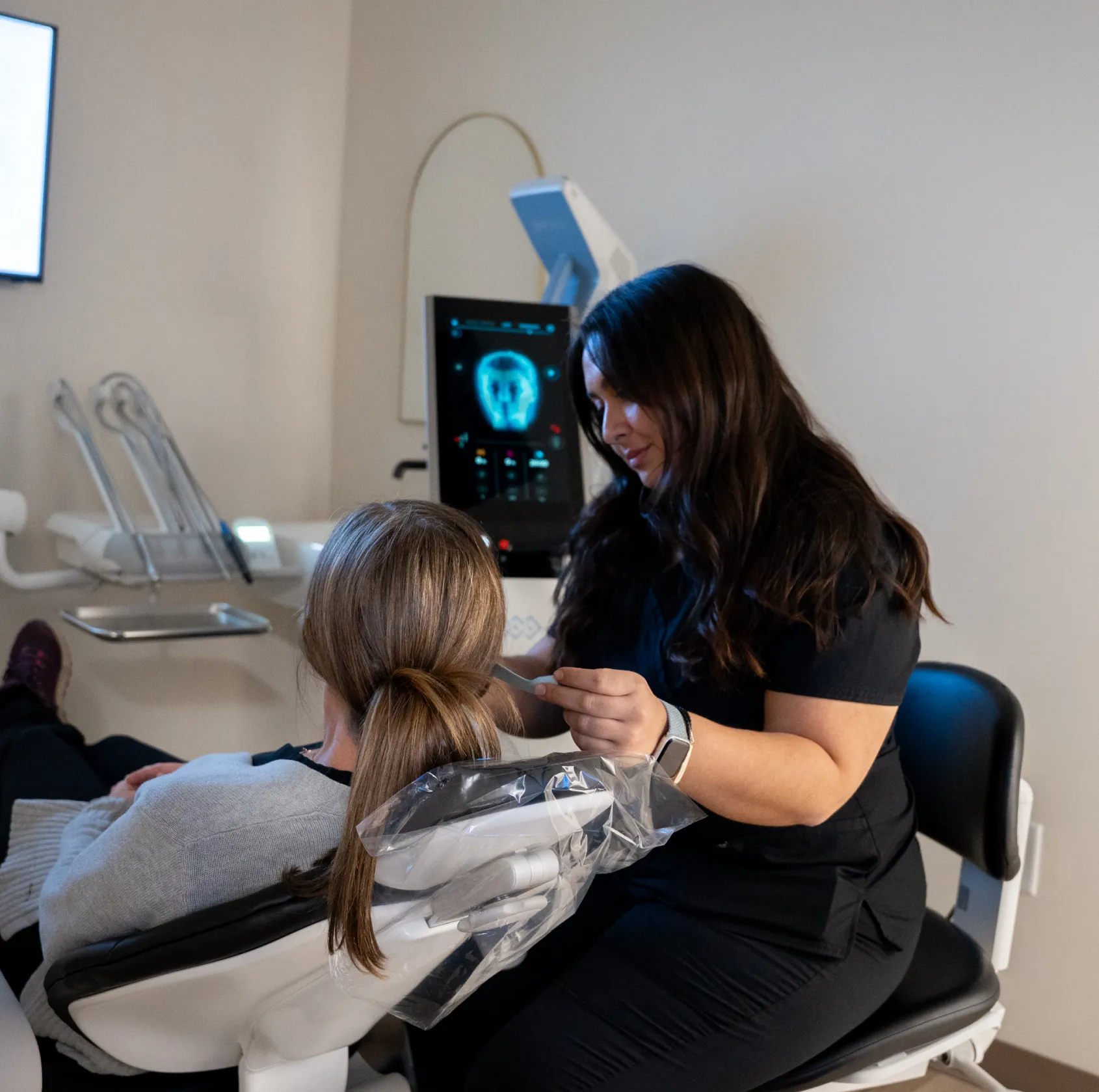 A dental professional assists a patient by examining their teeth using dental equipment.