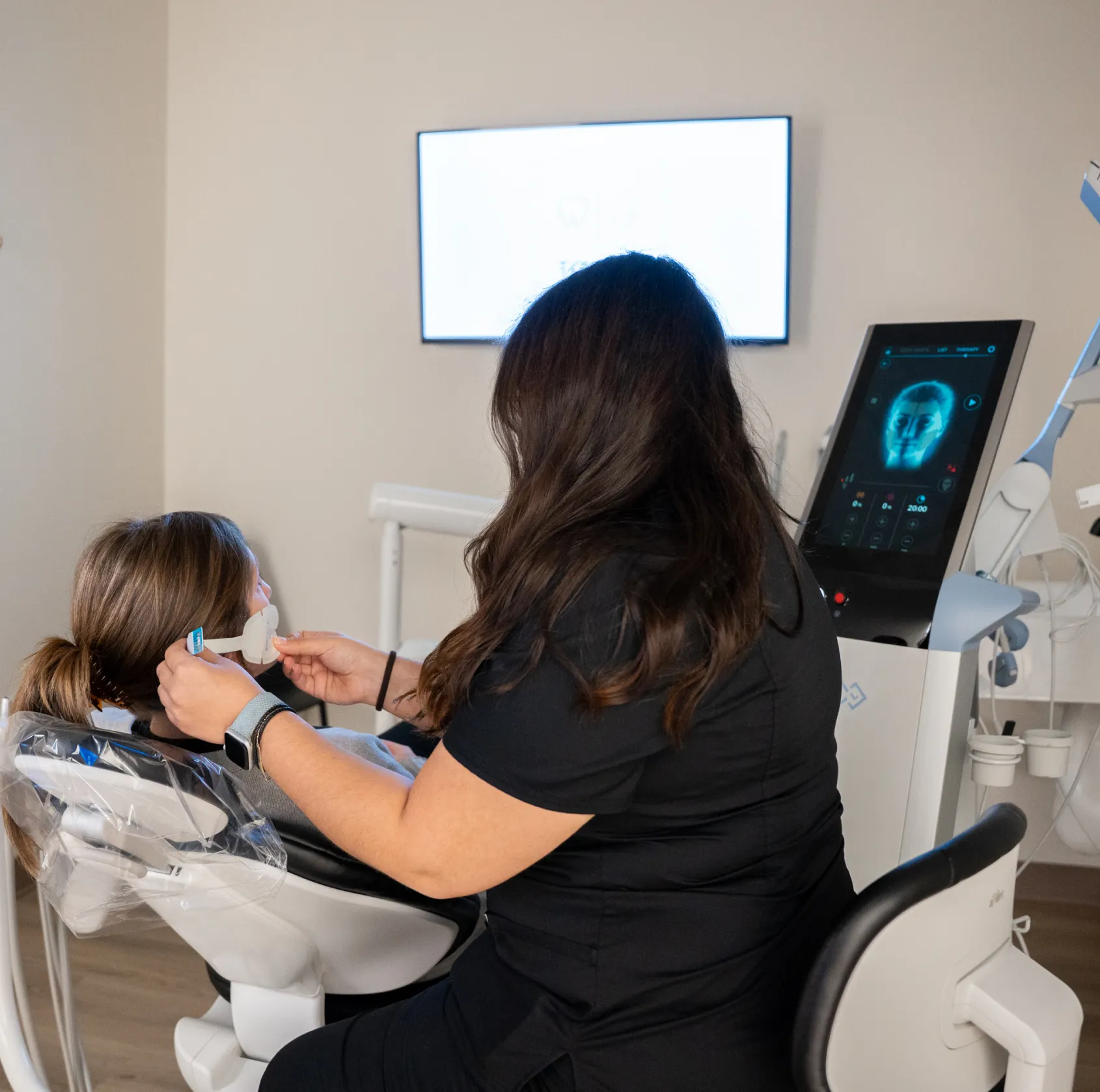 A dental professional adjusts a headset on a patient seated in a dentist's chair.