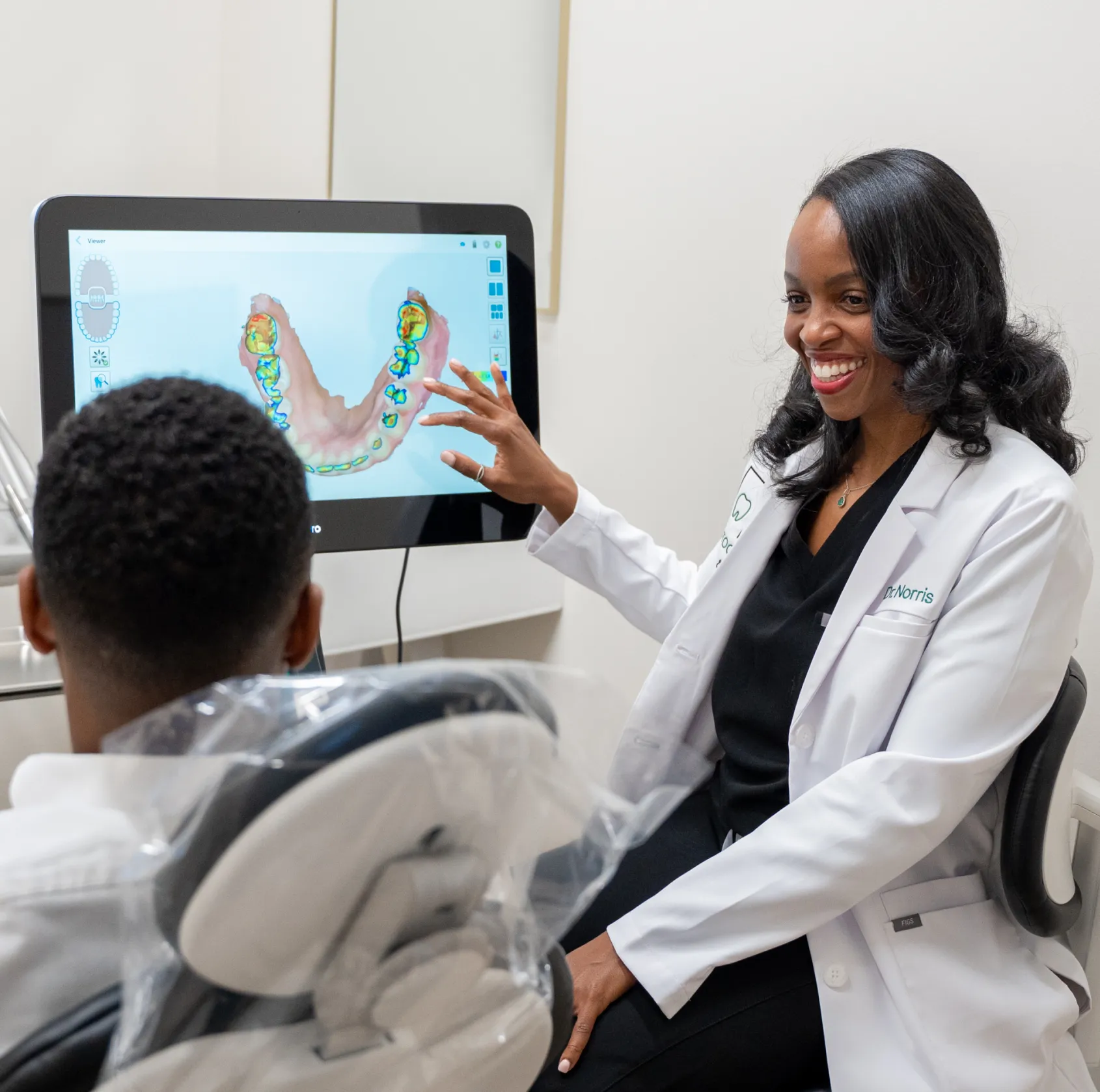 A dentist shows a dental scan on a screen to a patient in a consultation room.