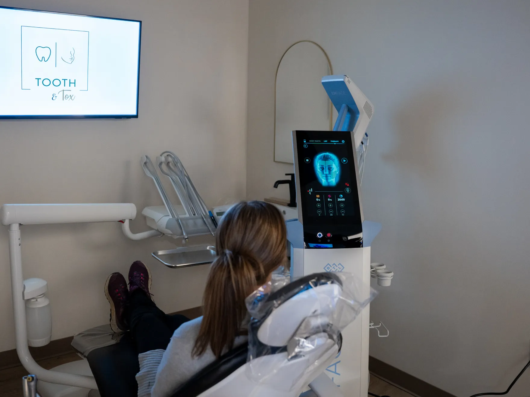 A person sits in a dental chair facing a screen displaying dental images and information.