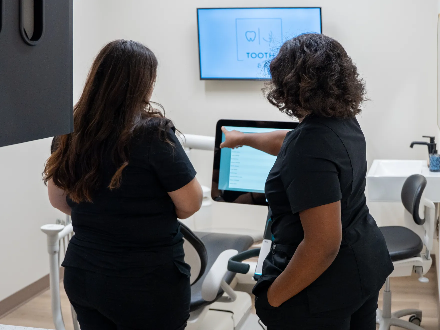 Two dental professionals discuss patient information on a computer screen in a dental office.