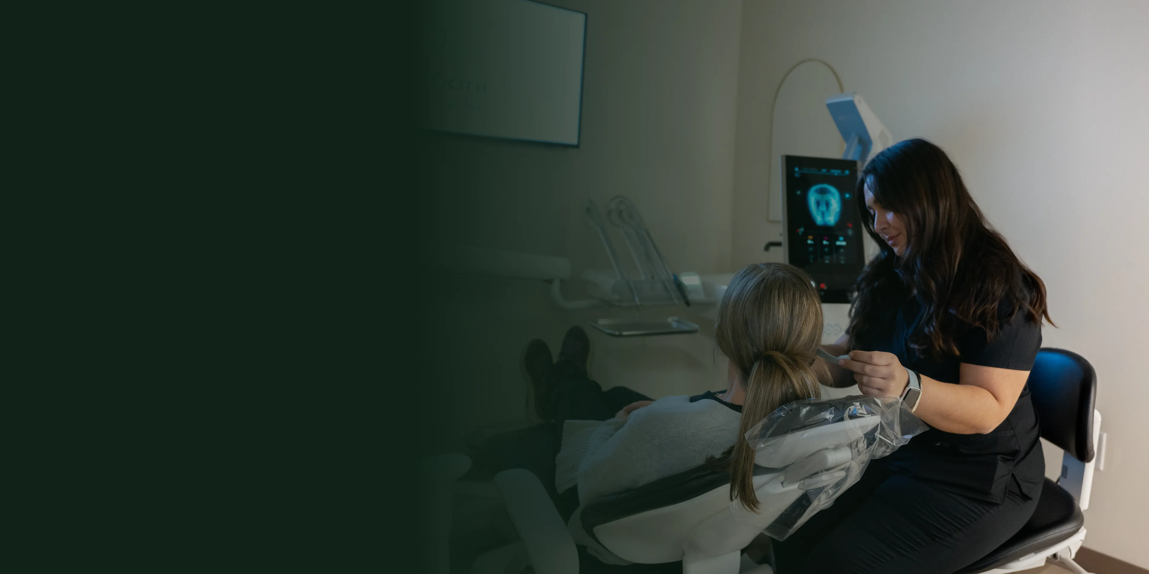 A dental professional talks to a patient in a dental office, with equipment visible nearby.