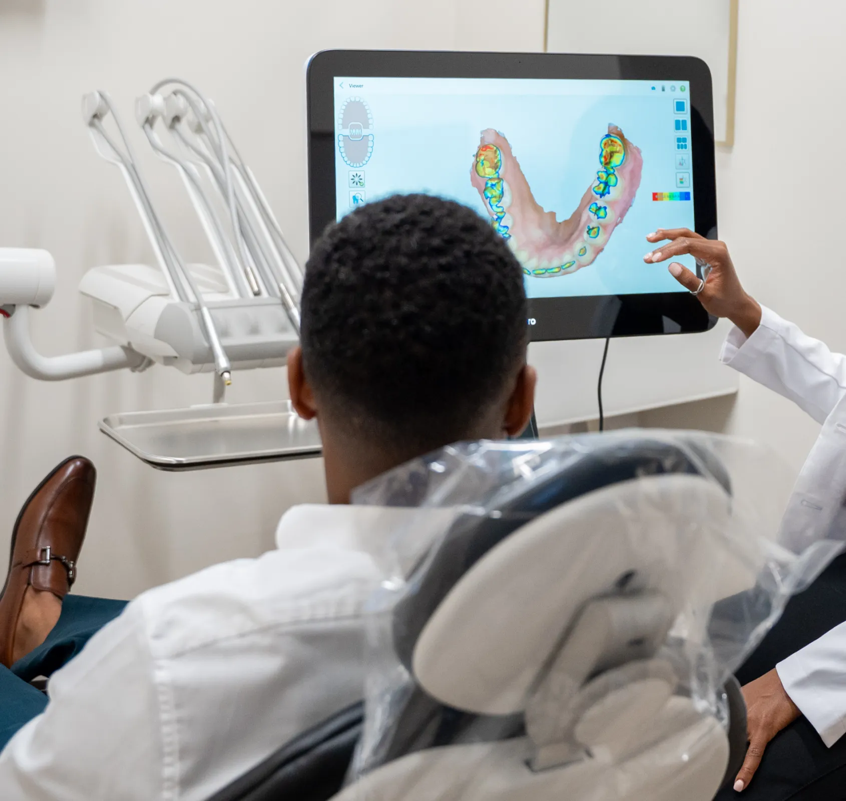 A dentist explains a dental scan image to a patient seated in a dental chair.