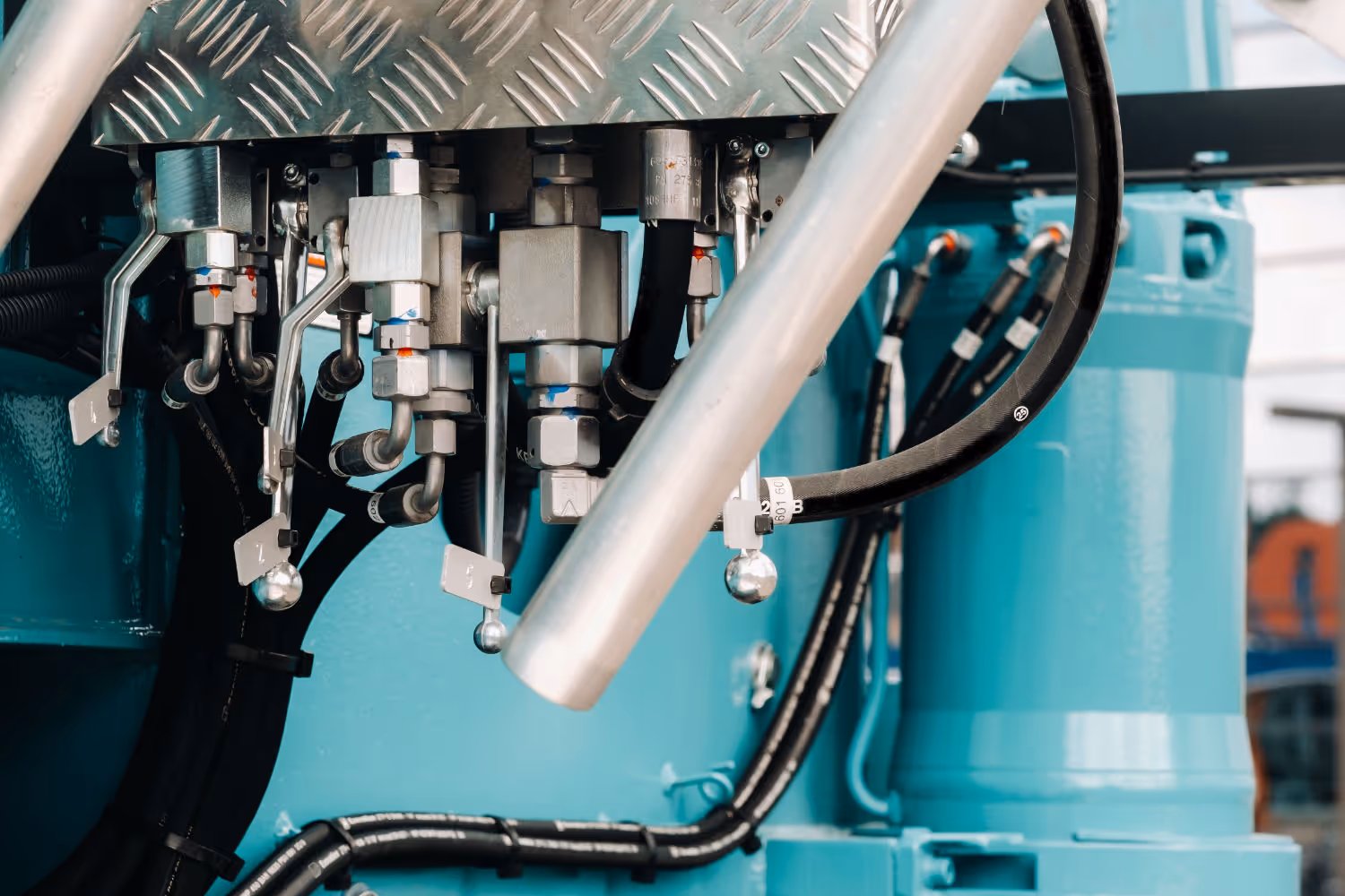 Hydraulisch systeem met metalen leidingen en slangen aan een blauwe machine.