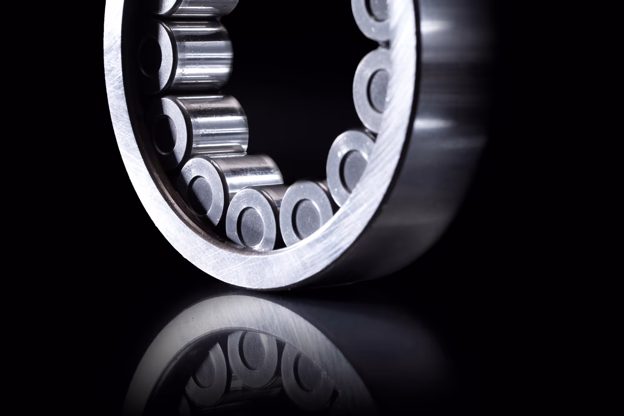 Close-up van een metalen kogellager met glanzende bolletjes en reflectie op zwart oppervlak.