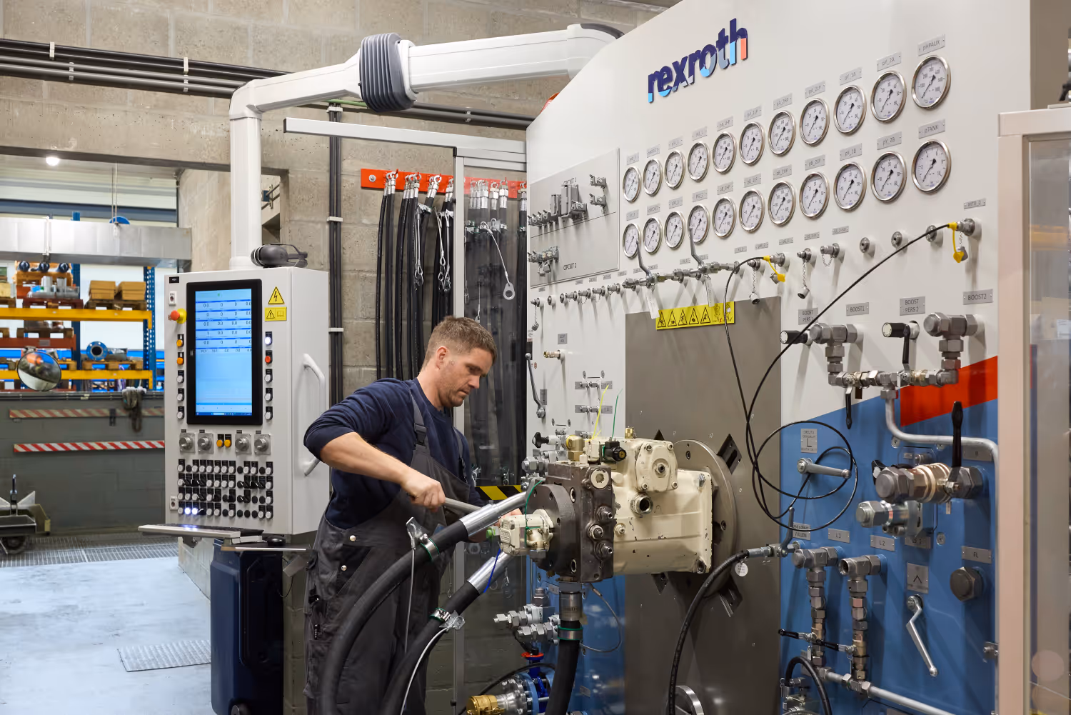 Technicus werkt aan een hydraulisch testsysteem met vele manometers en kleppen in een industriële omgeving.