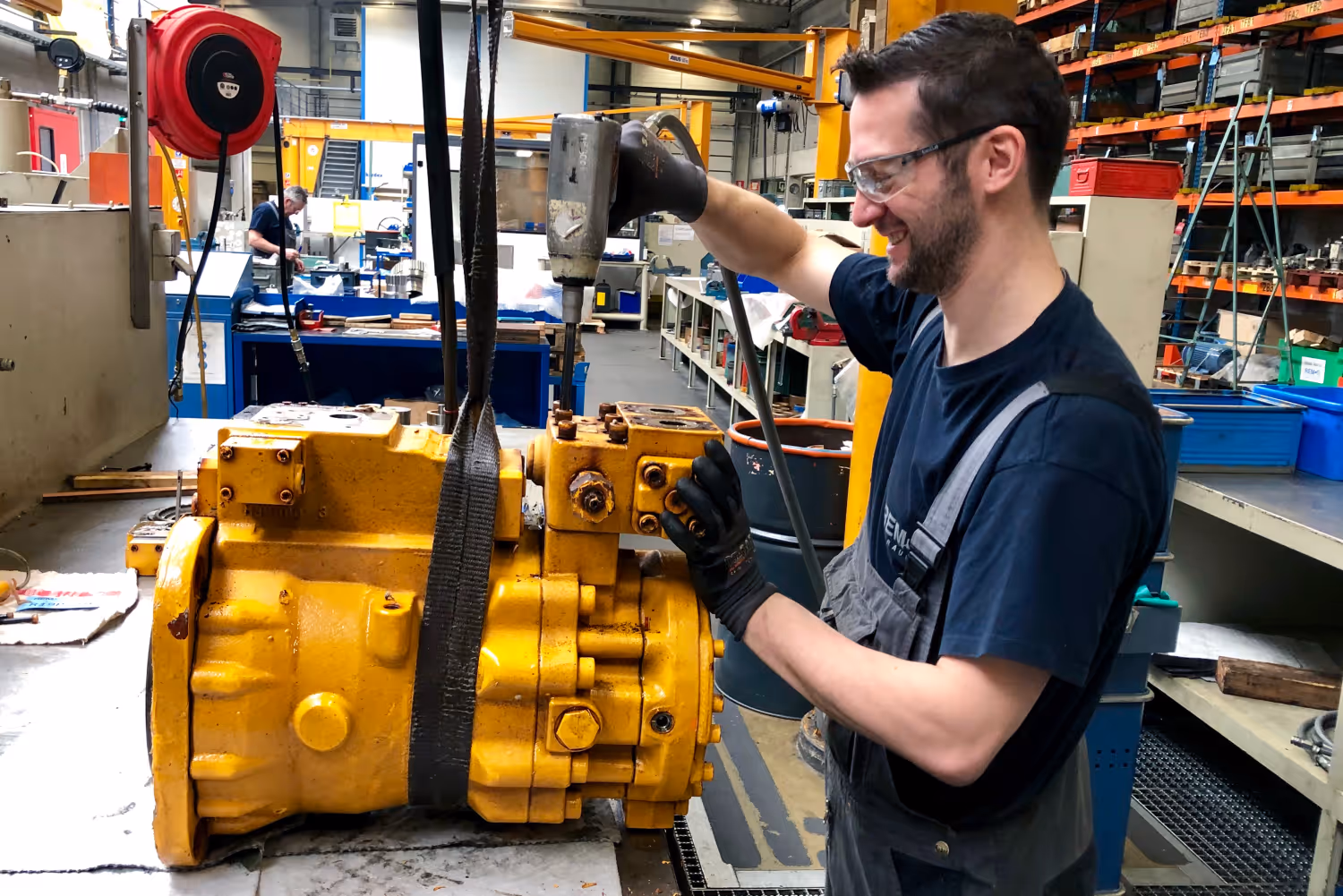 Man repareert een grote gele pomp in een werkplaats met gereedschap en machines.