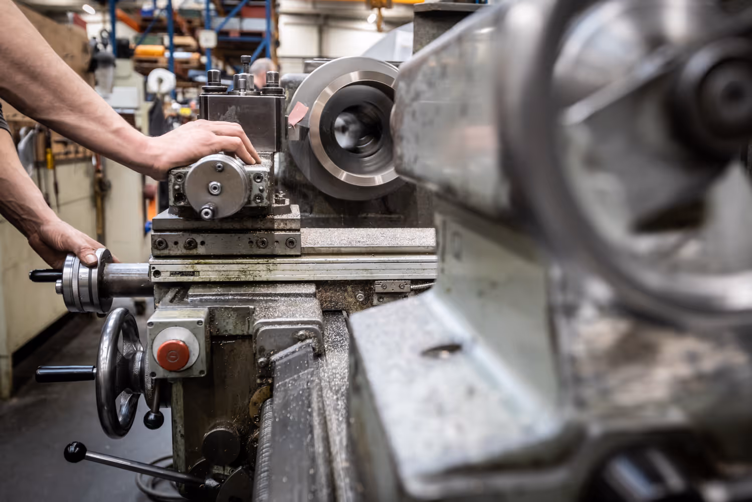 Hand bedient een metaalbewerkingsmachine in een fabriekshal met draaiende delen.