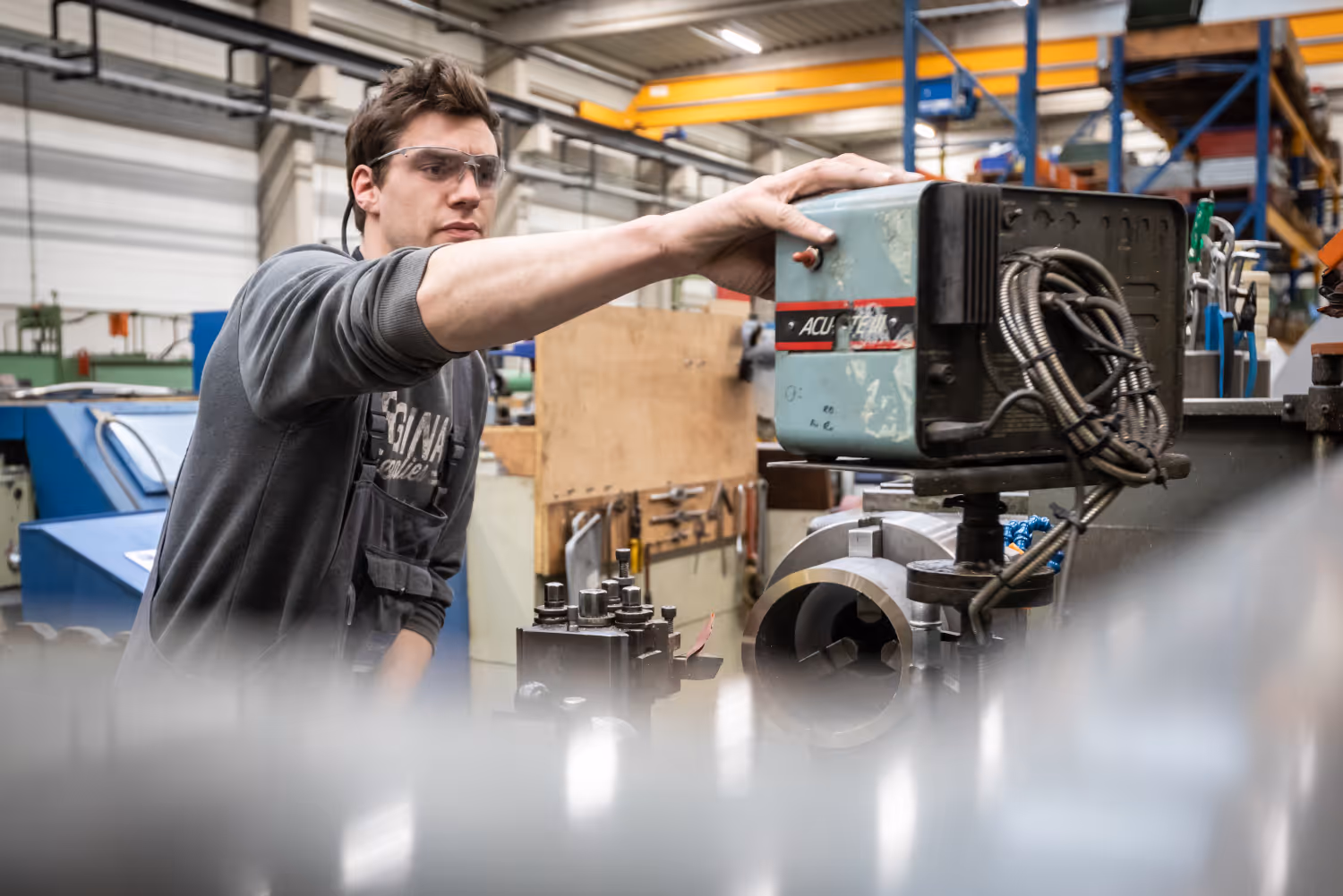 Man met veiligheidsbril bedient een industriële machine in een fabriekshal.