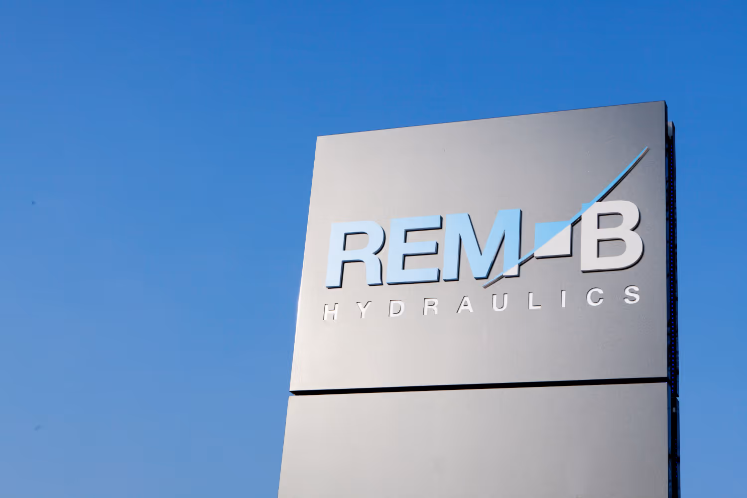 Bord met REM-B Hydraulics logo tegen heldere blauwe lucht.