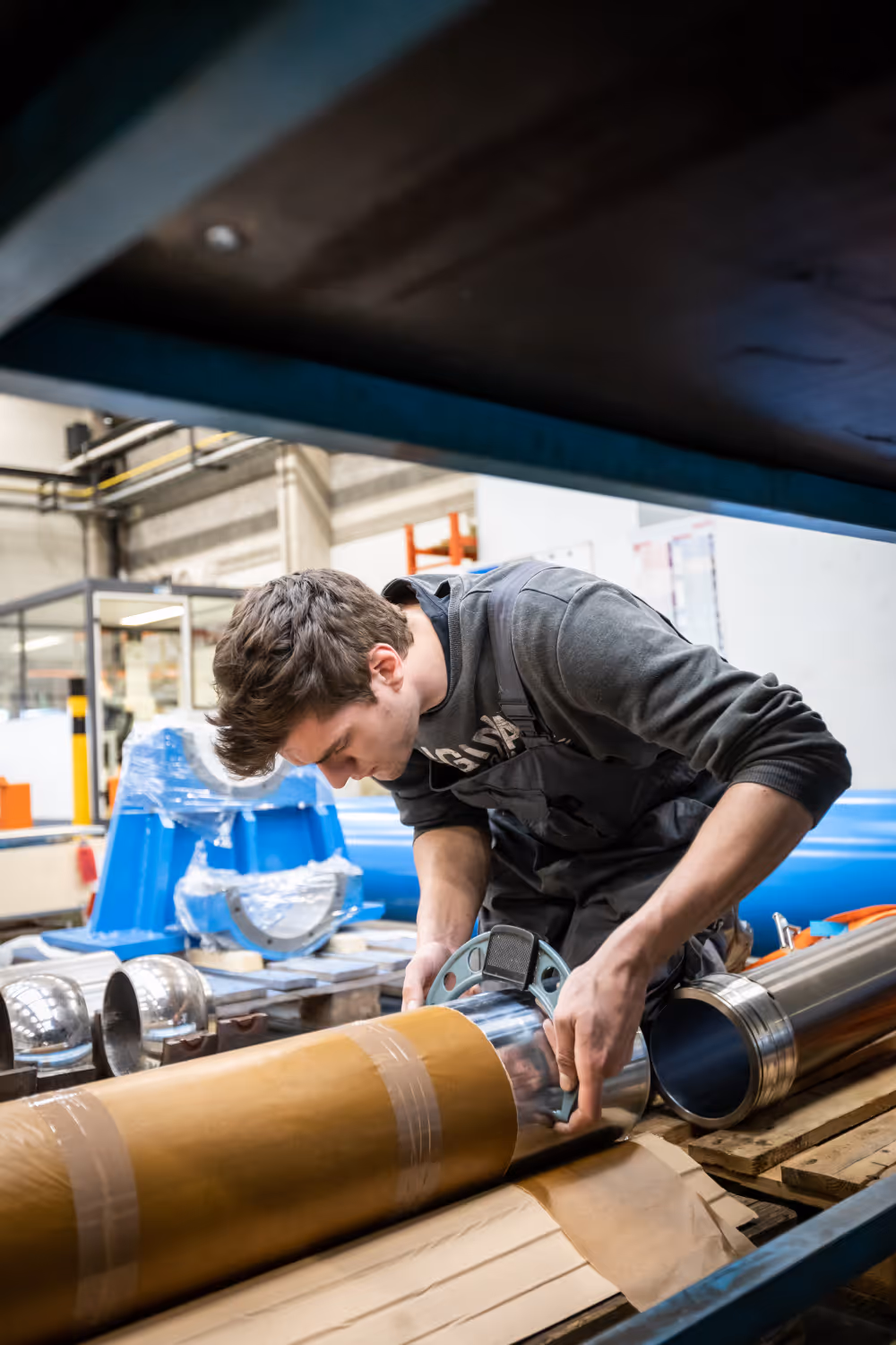 Man bevestigt metalen onderdeel aan buis in industriële werkplaats.