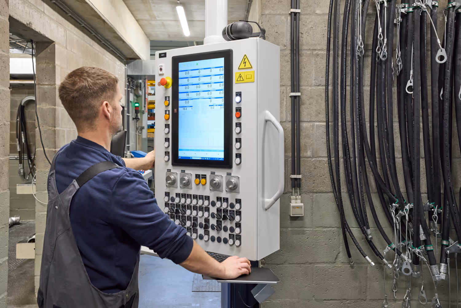 Technicus bedient een besturingspaneel met scherm en knoppen in een industriële omgeving.