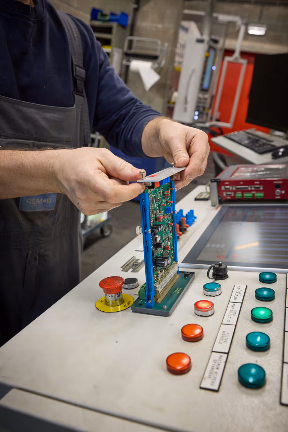 Technicus werkt aan een elektronisch circuitbord op een bedieningspaneel met knoppen en scherm.