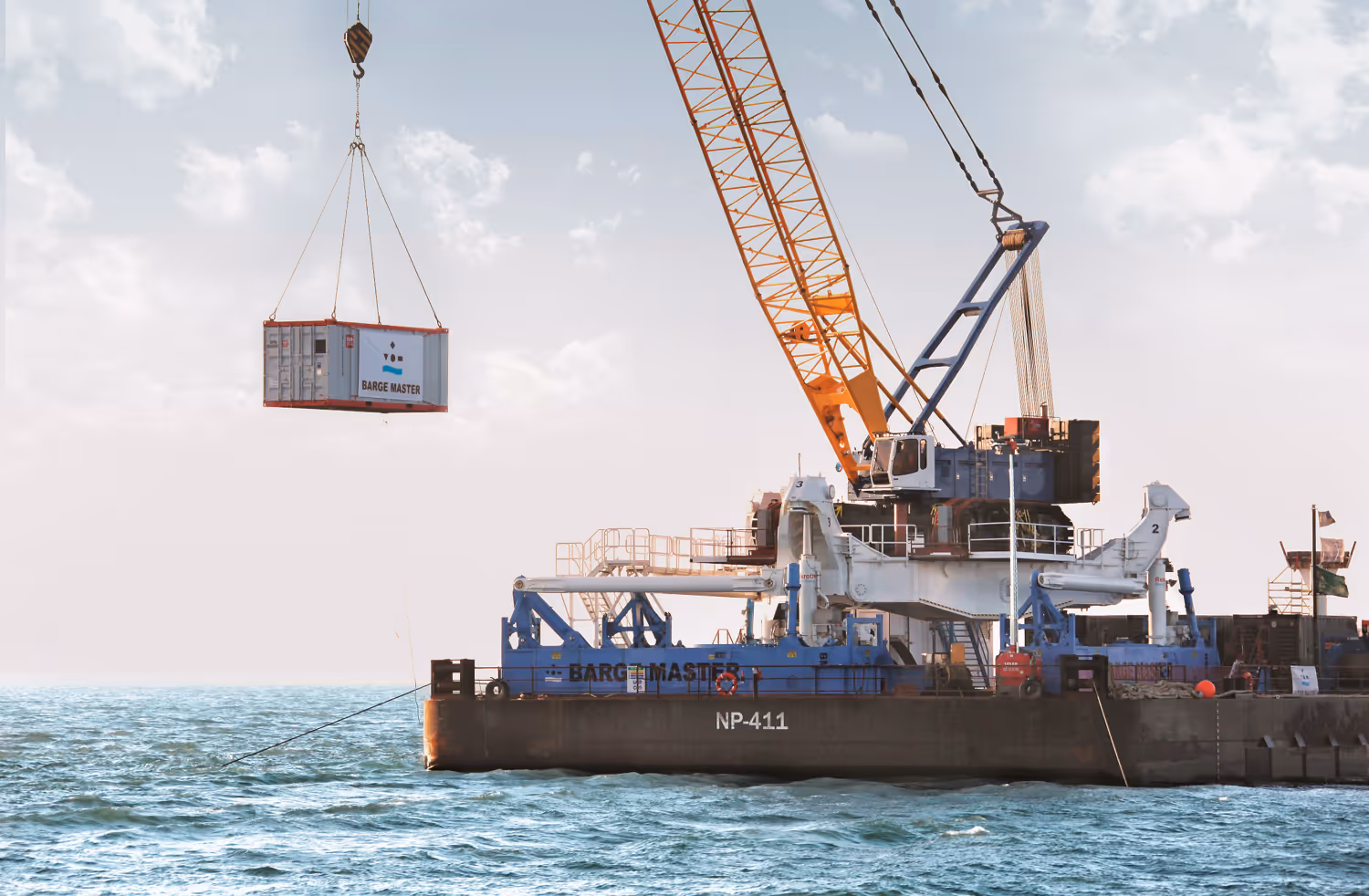 Een kraan op een ponton hijst een container boven de zee met de tekst Barge Master.