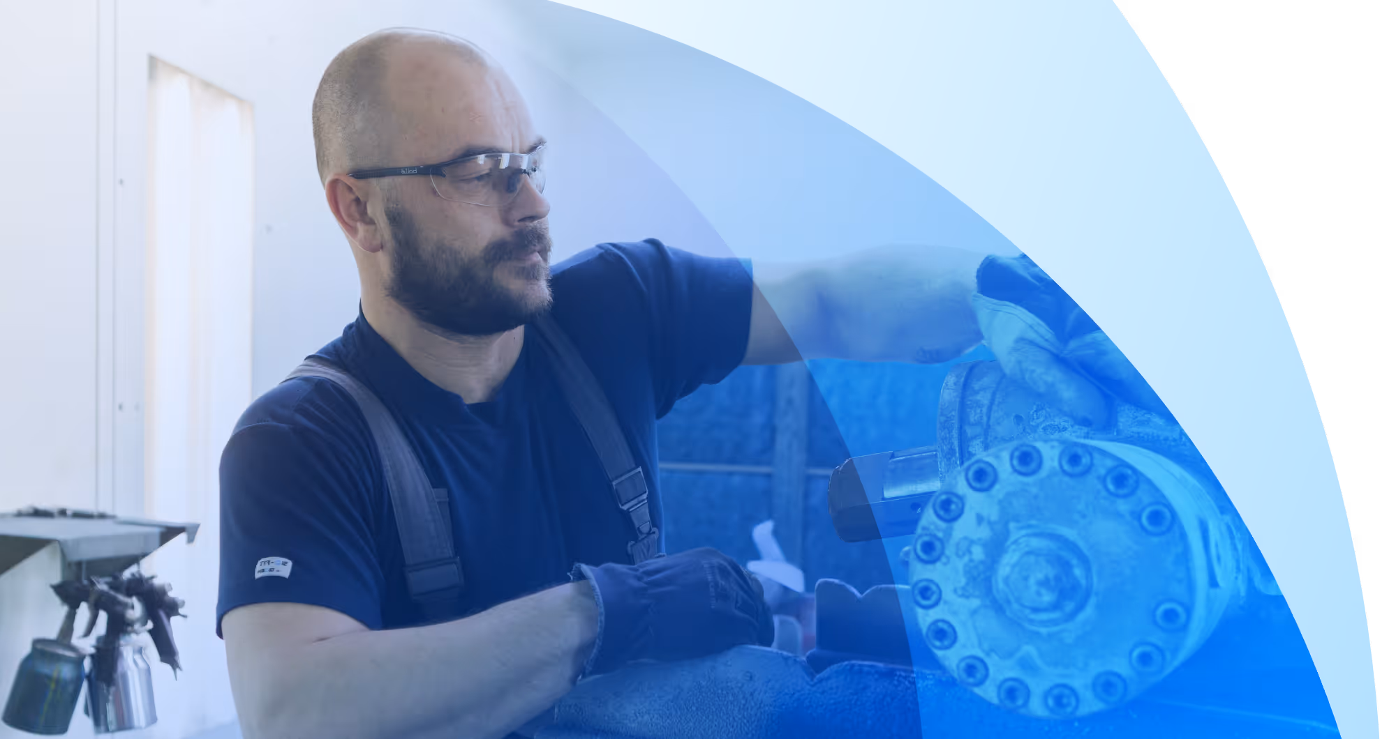 Man met bril en handschoen werkt met gereedschap in een lichte werkplaats.