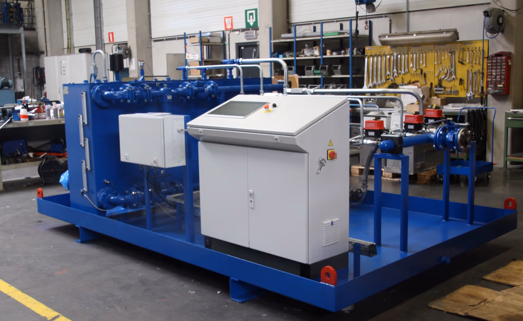 Blauwe industriële machine met wit bedieningspaneel in een werkplaats met gereedschap en materialen.