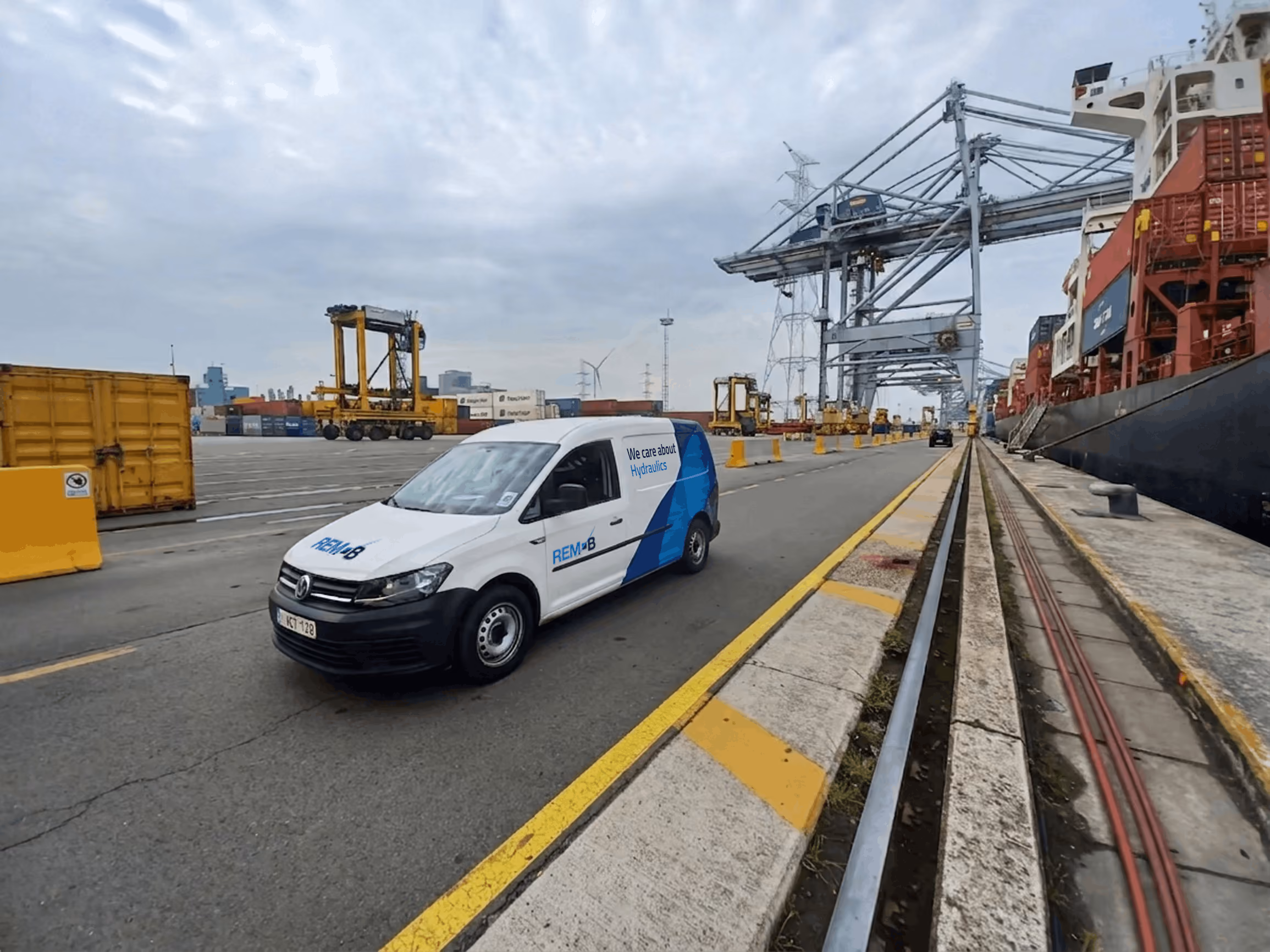 Witte REMAB bestelwagen op een bedrijvige containerterminal naast een groot vrachtschip.