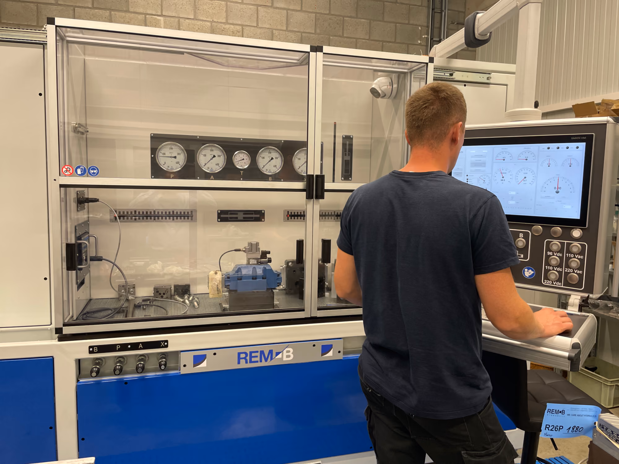 Een man bedient een testmachine voor ventielen met meerdere meters en een digitaal scherm in een industriële omgeving.