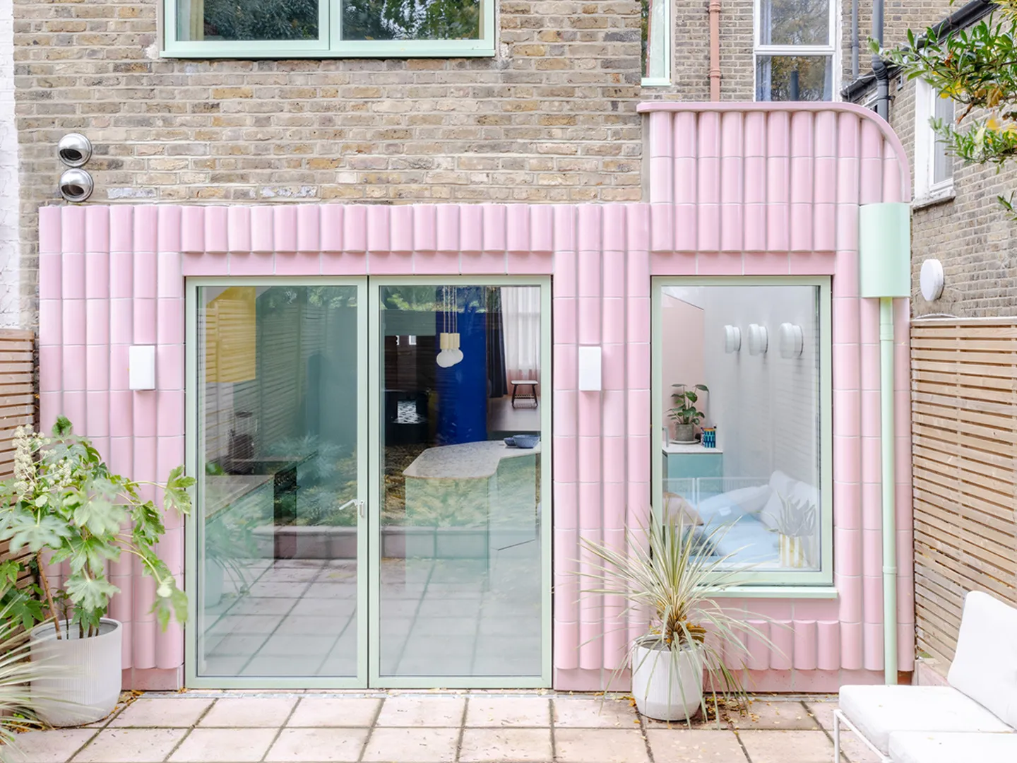Photo showing the entirety of the project with its pink facade elements, looking into the space inside. By Office S&M, RIBA Chartered Architectural Practice in London