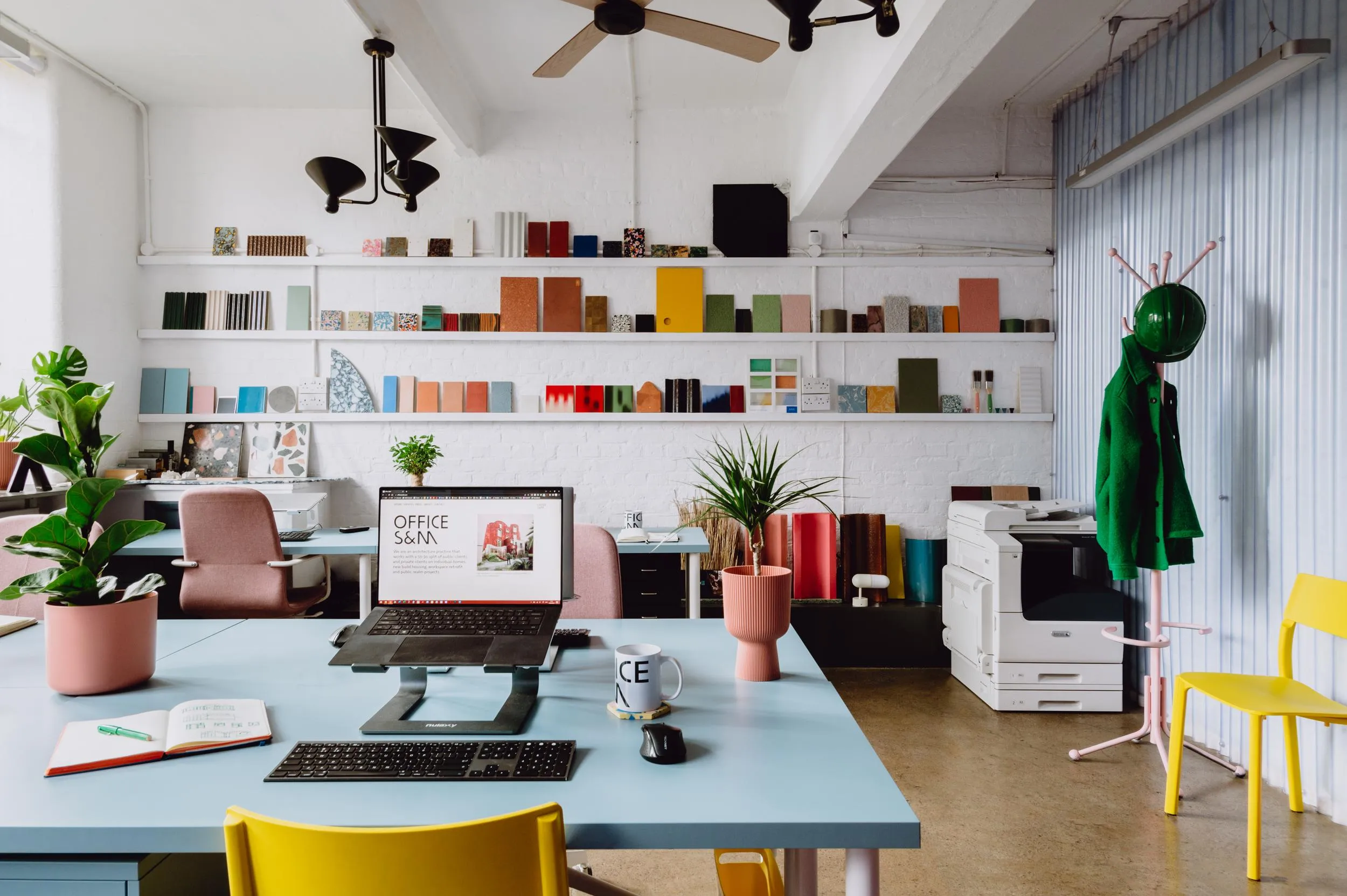 Overview photo of the working space, showing the arrangement of desk, computers with a long shelving units in the background. By Office S&M, RIBA Chartered Architectural Practice in London.