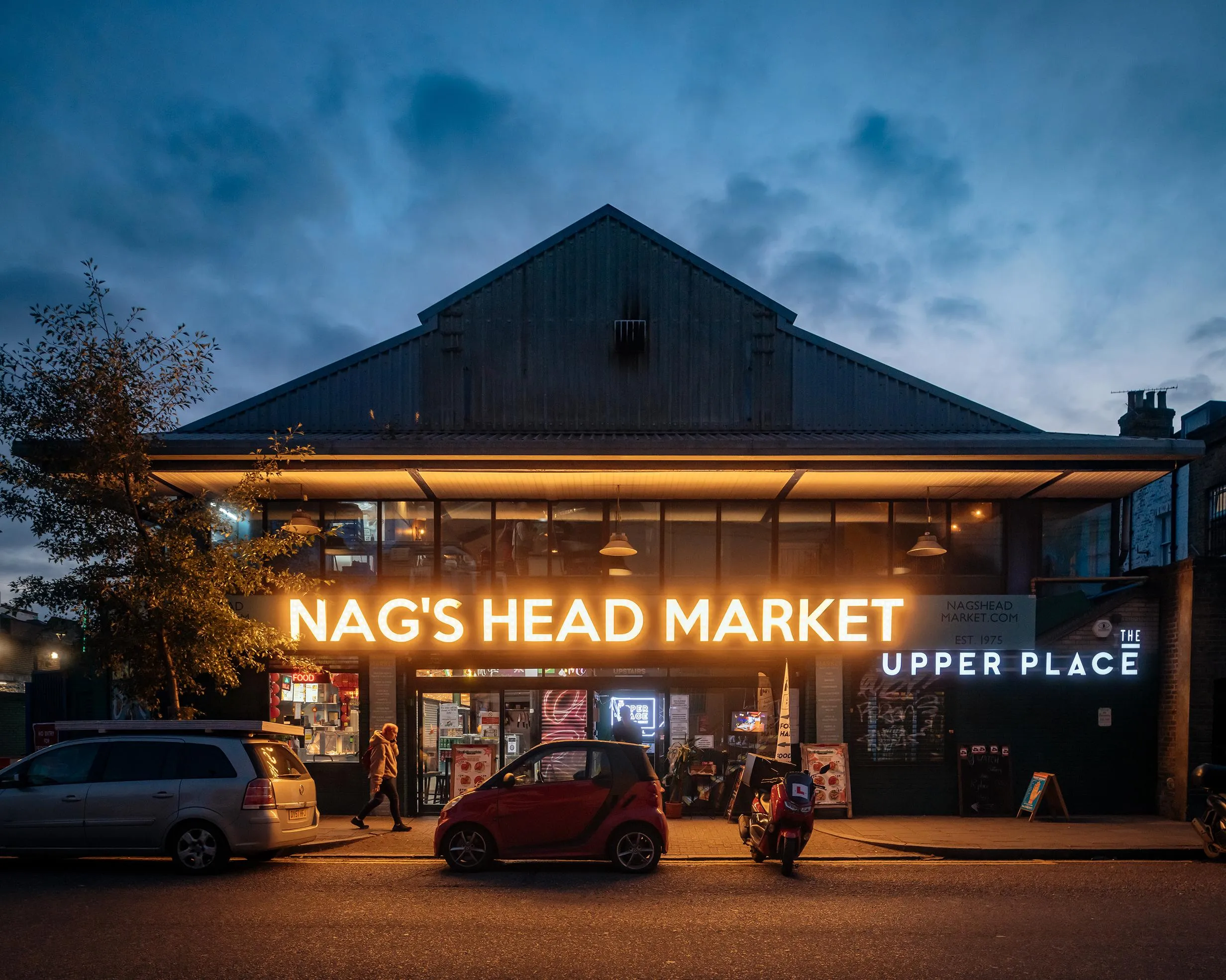 Photo of Nag's Head market at dusk, with the sign illuminated. By Office S&M, RIBA Chartered Architectural Practice in London.