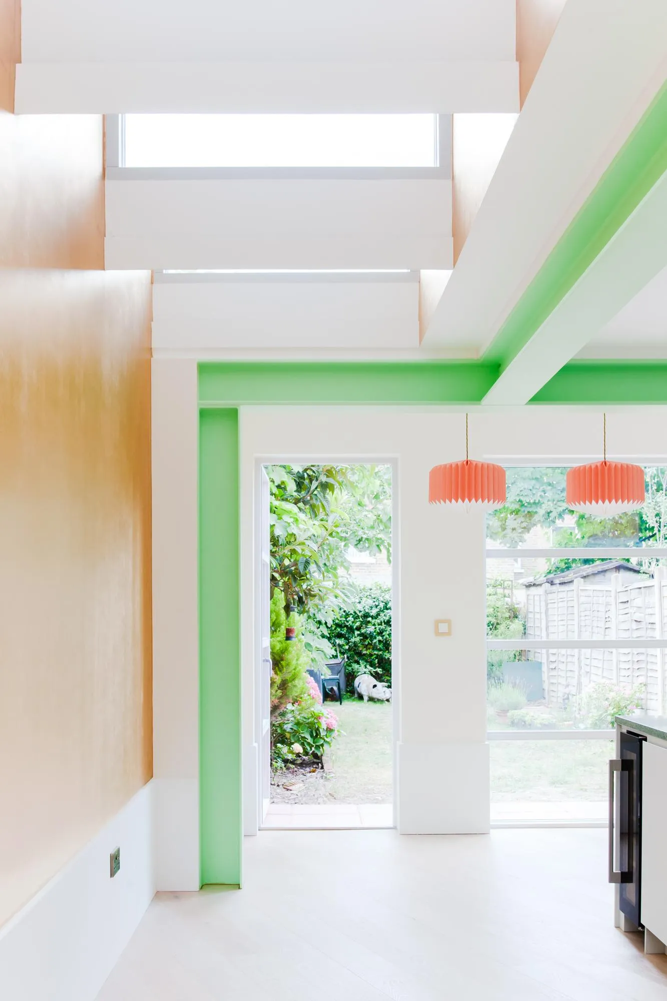 Internal photo of the space with green beams, with garden in the background. By Office S&M, RIBA Chartered Architectural Practice in London.