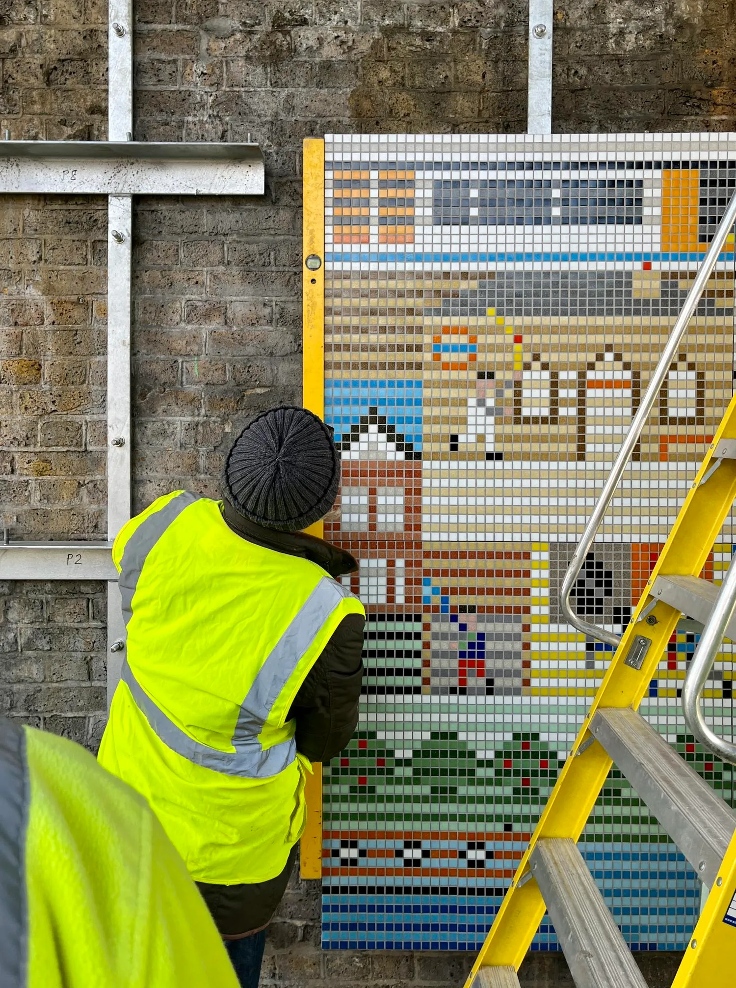 Woman in a high vis jacket installing the mural. By Office S&M, RIBA Chartered Architectural Practice in London.
