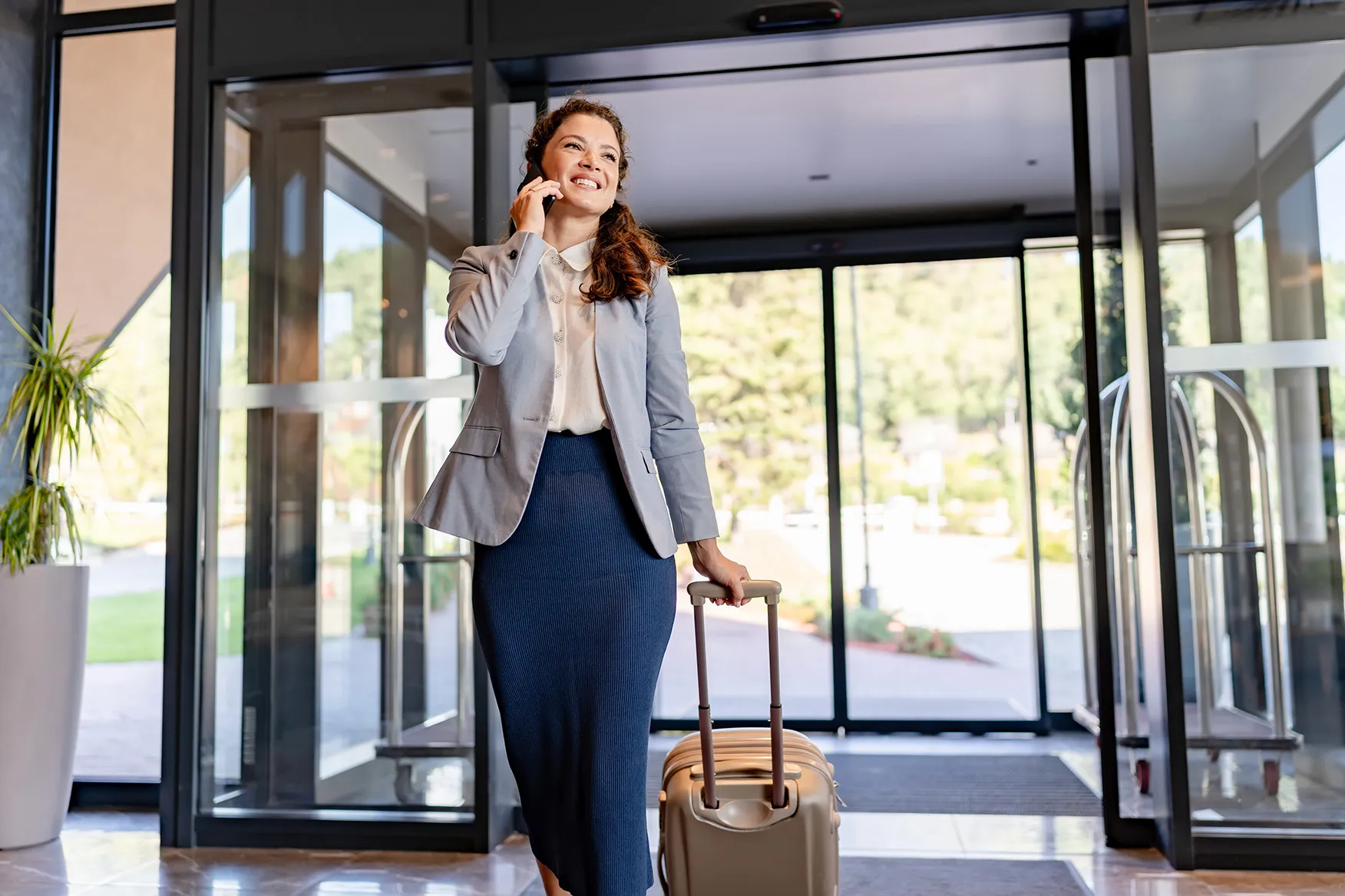Woman with a big smile entering a lobby while holding her suitcase
