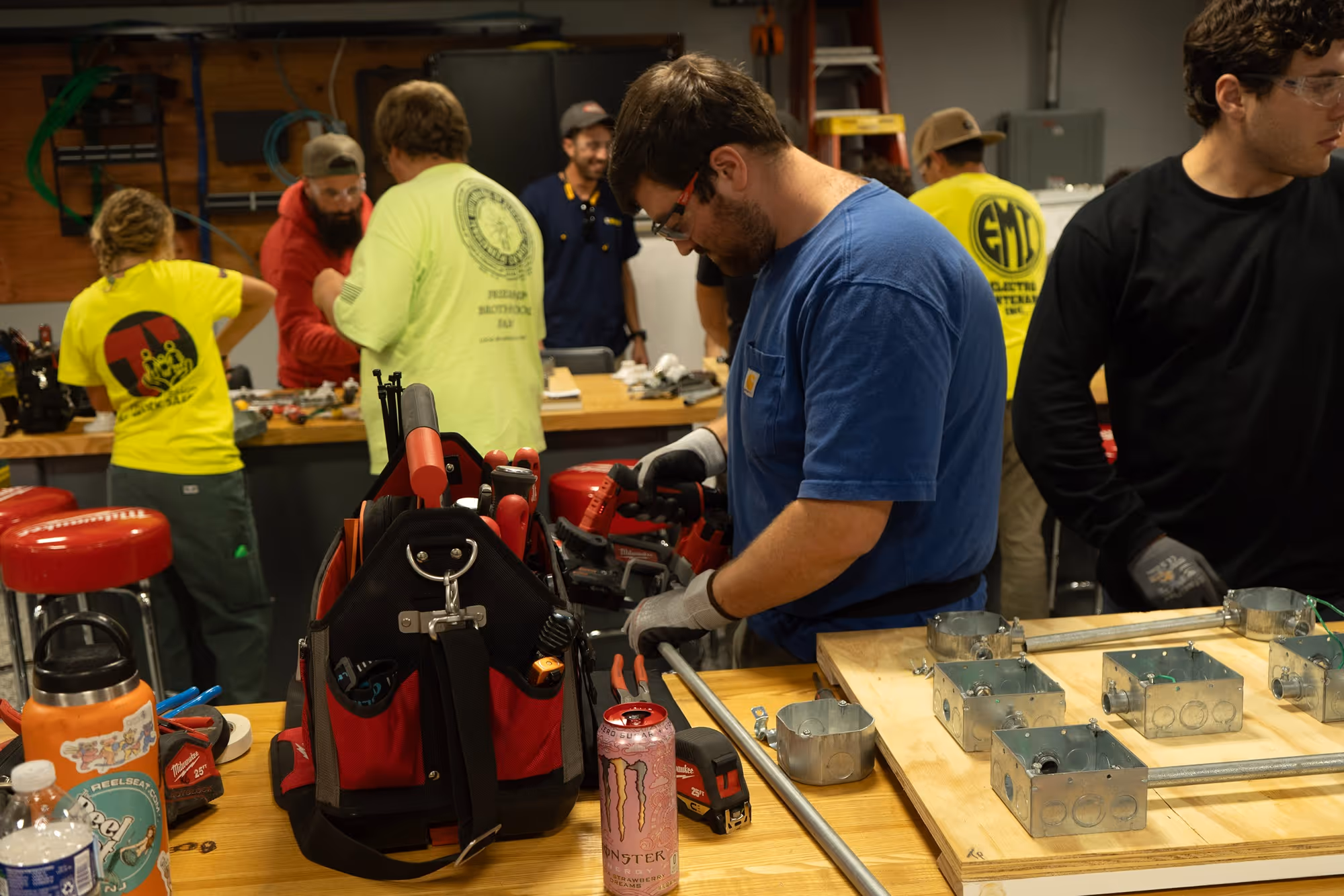Group of people working on electrical wiring and assemblies on wooden tables in a workshop.
