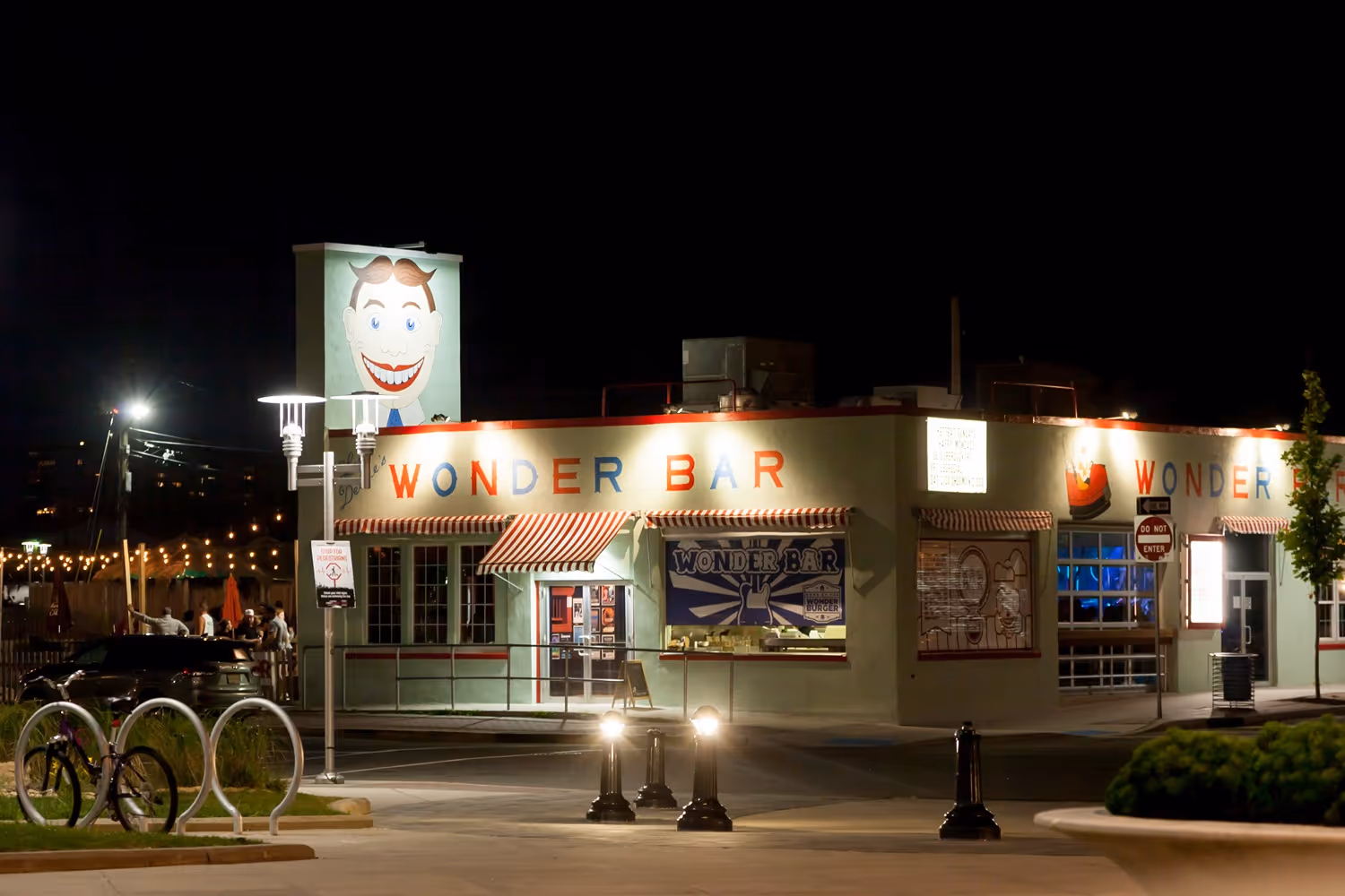 Night view of Wonder Bar building with illuminated sign and a large smiling face mural on top, featuring outdoor string lights and a bicycle rack in front.