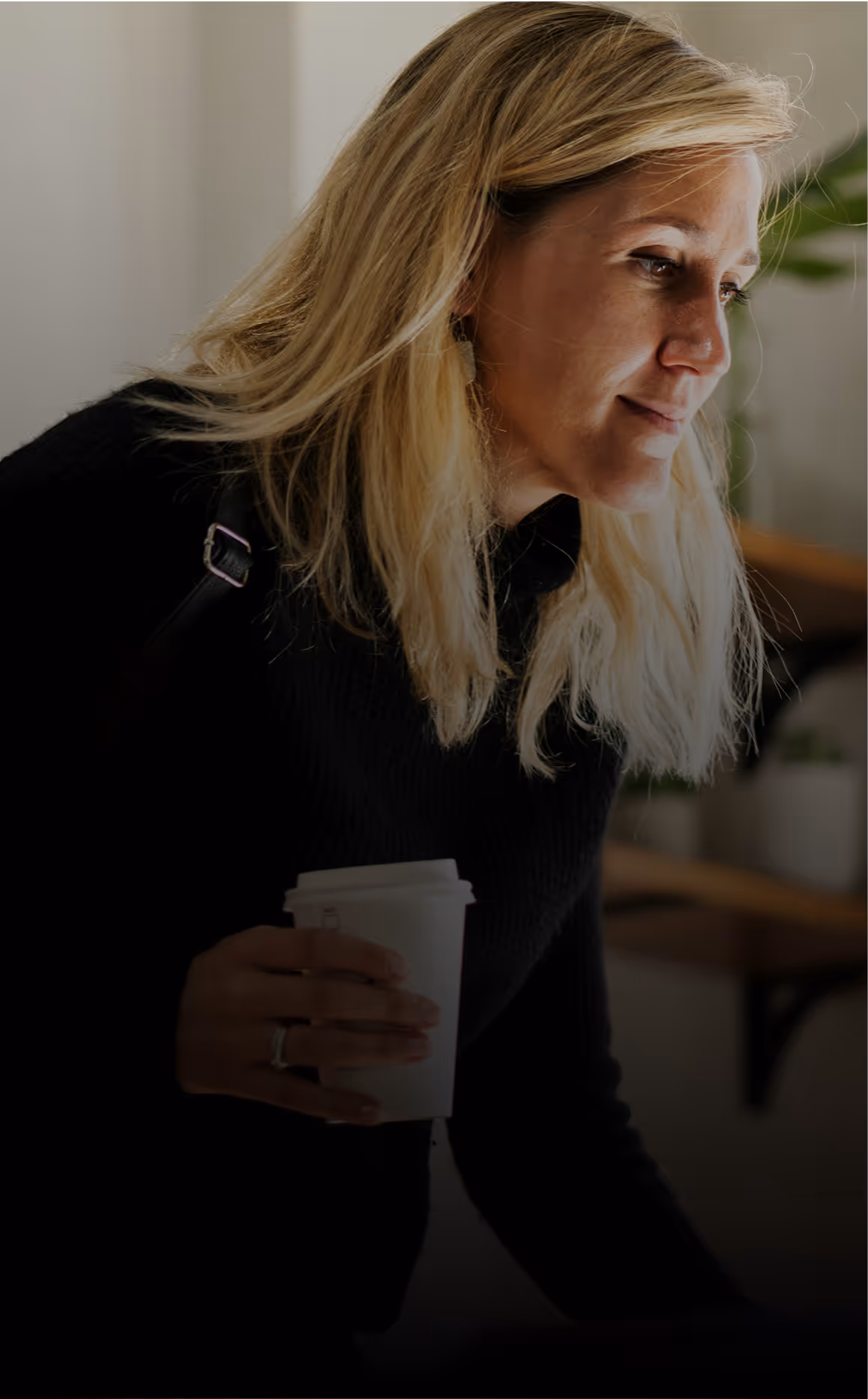 Thoughtful woman in black holding coffee, ready to opine on workplace challenge