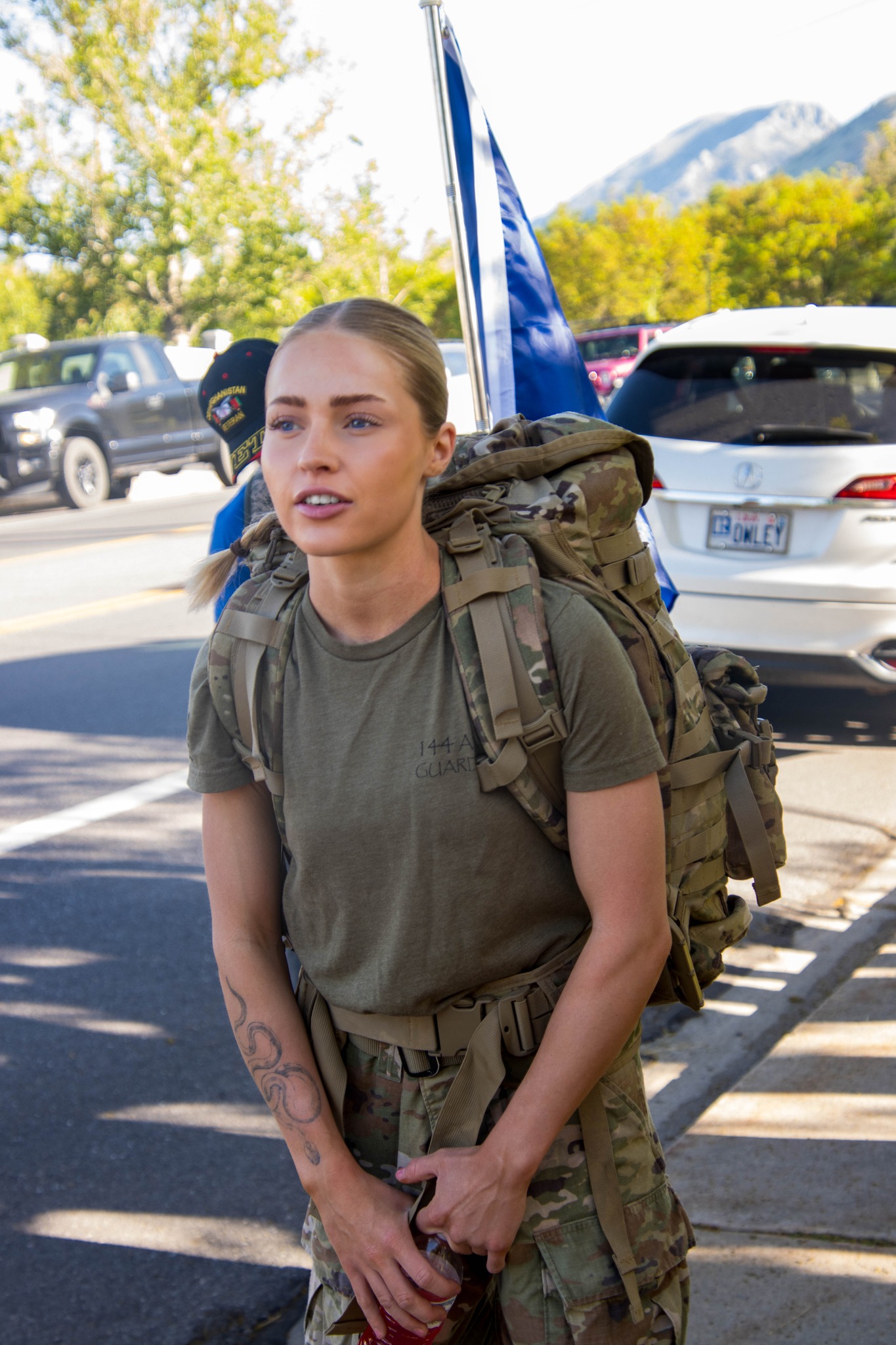Female soldier with backpack and tattoo stands on street during event