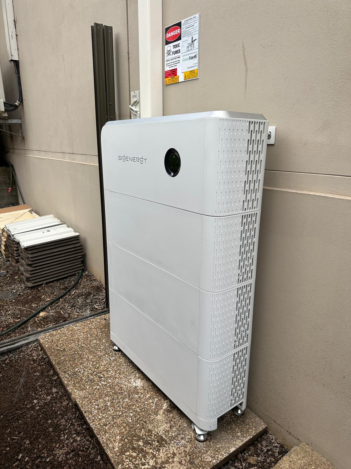 White SIGENERGY energy storage battery unit installed outdoors on a concrete slab against a beige wall.