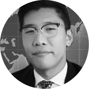 Black and white portrait of a man wearing glasses, a suit, and tie, with a world map in the background.