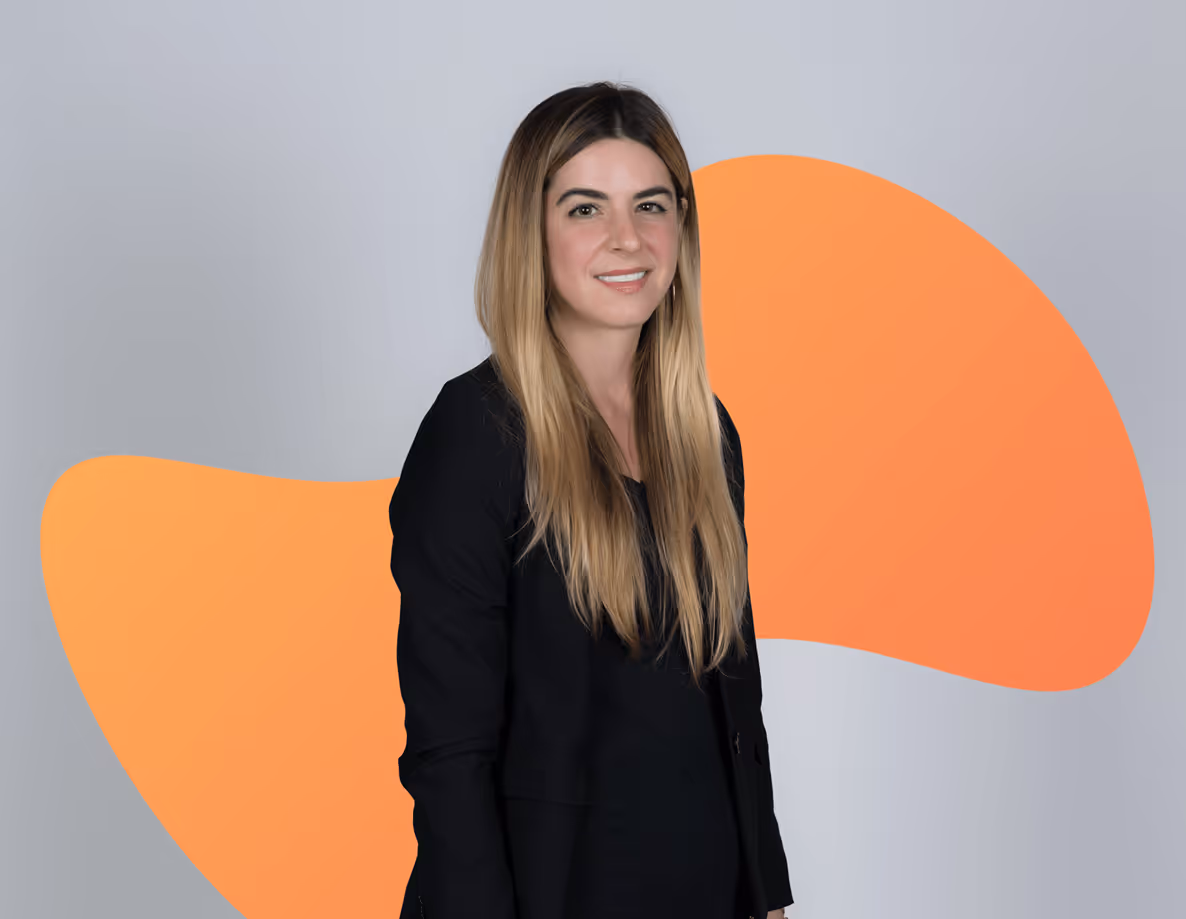 Smiling woman with long blonde hair wearing a black blazer against a gray background with orange abstract shapes.